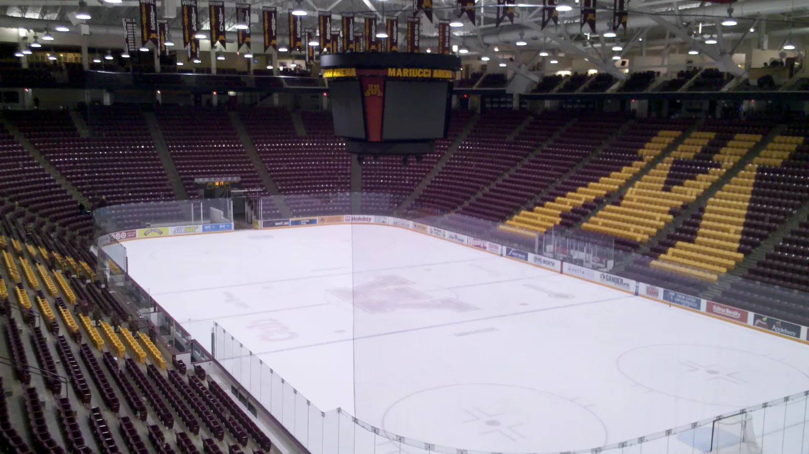 La pista vacía vista desde las gradas, con la M de los Gophers en el centro del hielo, el marcador colgado al centro y los asientos color granate y dorado. Fotografiada en noviembre de 2012, antes de la renovación de 2023 que redujo la pista. — 3M Arena at Mariucci