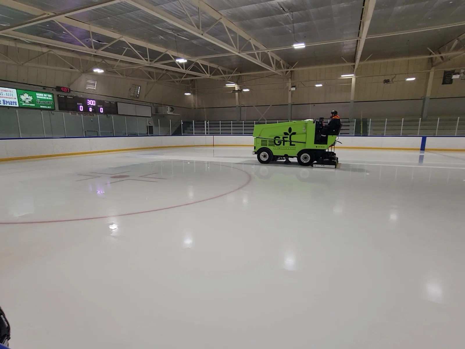 La pista vacía con la pulidora de hielo verde trabajando y las gradas detrás del vidrio. — Adie Knox Herman Arena