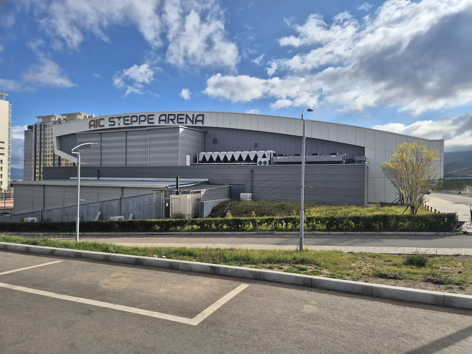 AIC Steppe Arena seen from the car park, a curved grey and white arena building with its name along the top of the facade — AIC Steppe Arena