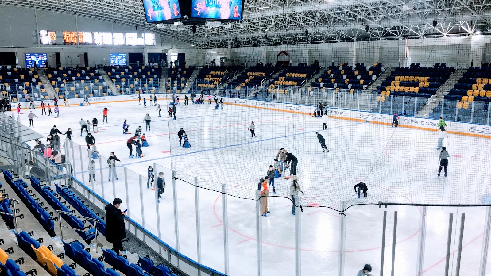 A public skating session on the ice of the AIC Steppe Arena in Ulaanbaatar, seen from the stands with skaters across the sheet. — AIC Steppe Arena