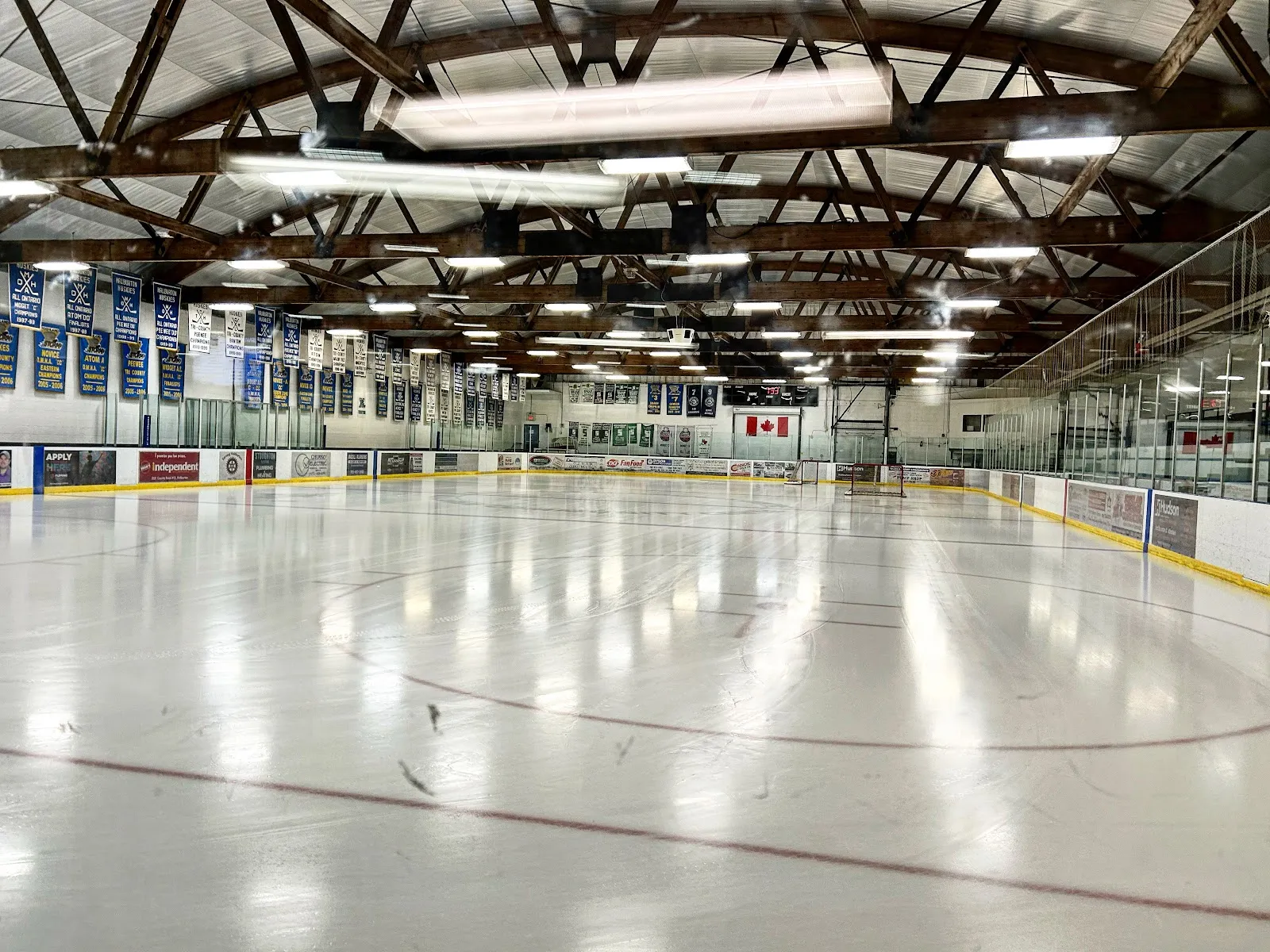 The empty ice surface inside the A.J. LaRue Arena, with the wooden roof trusses and the banners along the wall — A.J. LaRue Arena