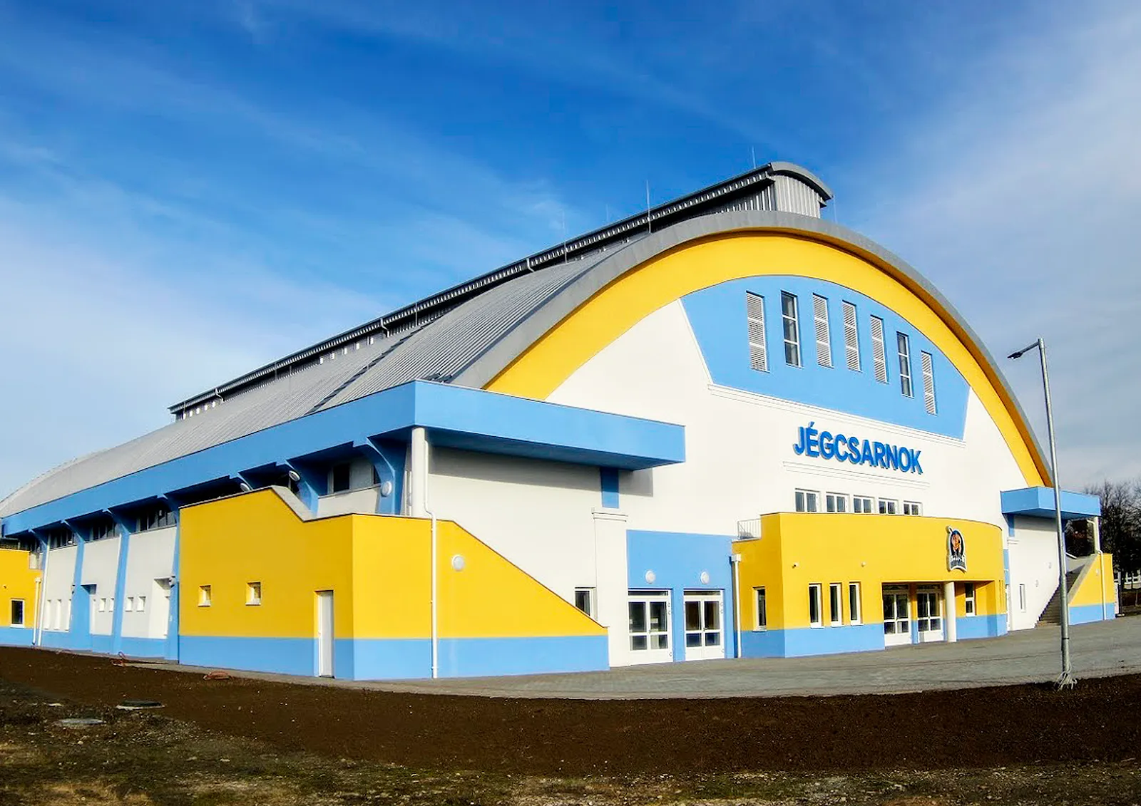 The Ajka Jégcsarnok building, with its arched yellow-and-blue front and the JÉGCSARNOK sign above the entrance — Ajka Jégcsarnok