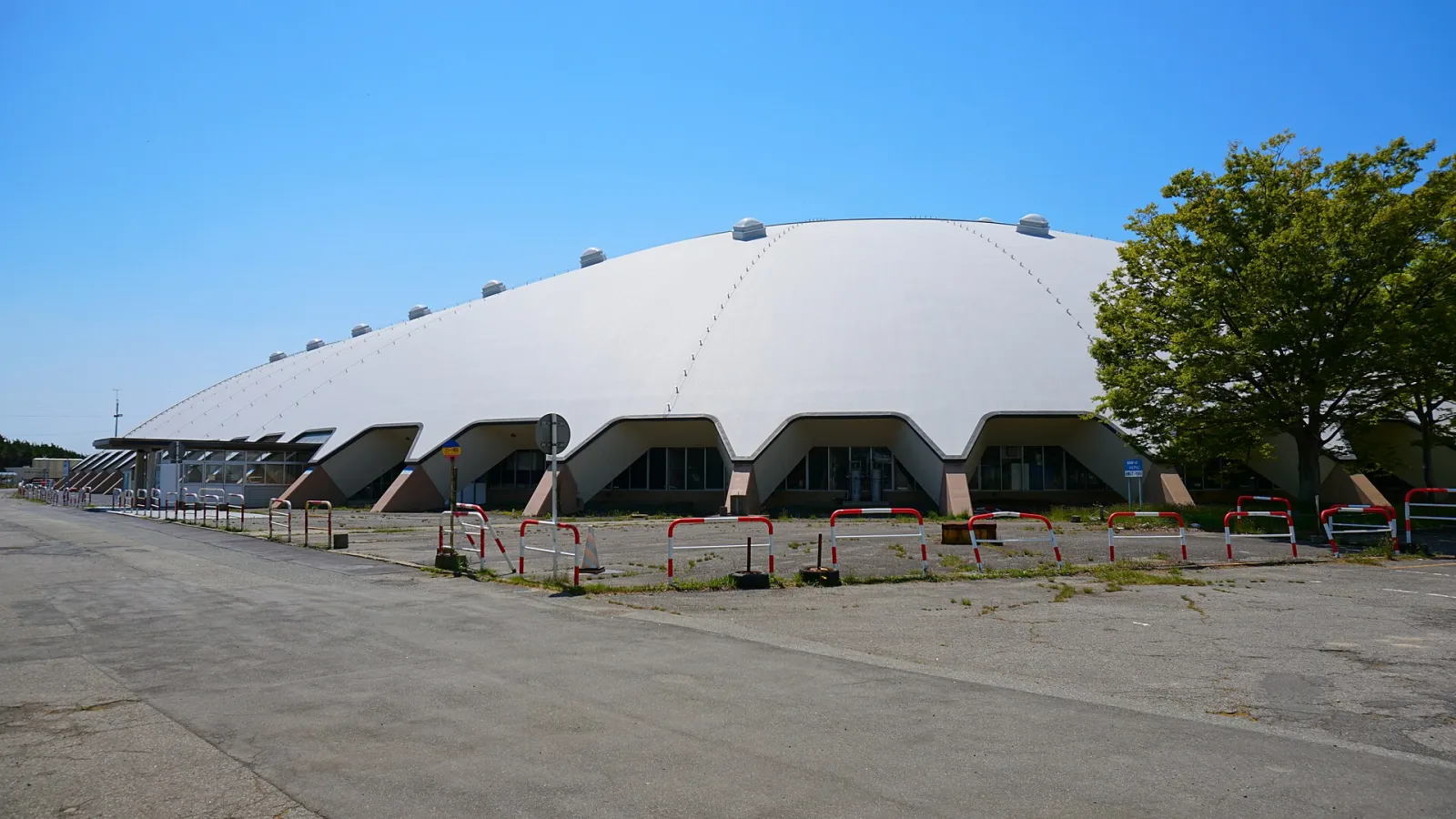 晴れた日に、駐車場側から見た秋田県立スケート場の長い白いドーム屋根。 — Akita Prefectural Skating Rink