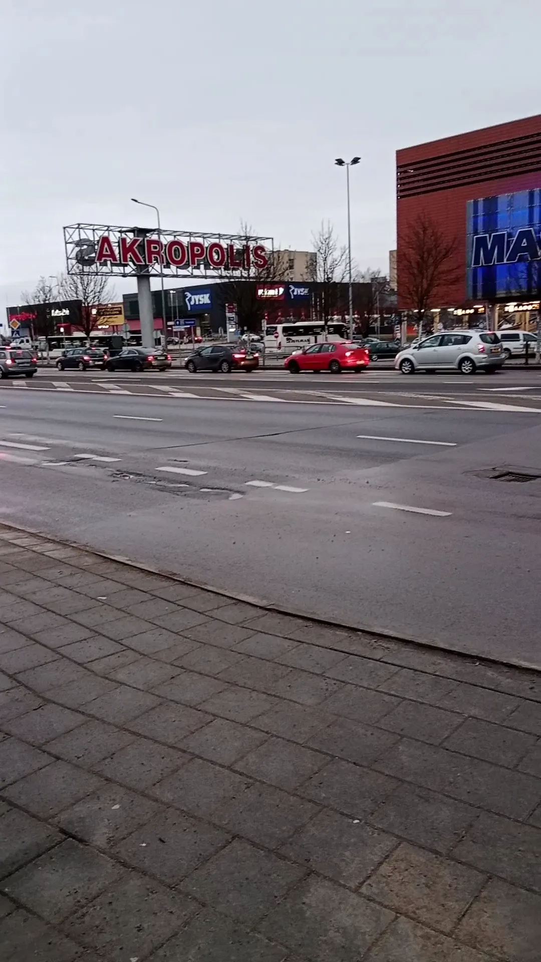 Akropolio Šiaulių prekybos centras, pastatas, kuriame veikia čiuožykla, matomas per Aido gatvę, su raudonu AKROPOLIS užrašu ant stiebo. – Akropolio ledas Šiauliuose