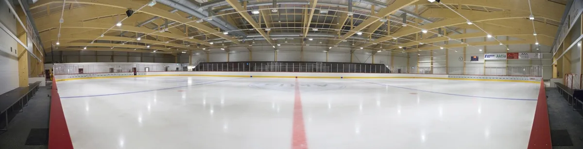 The empty ice sheet of Aktia Ishall seen along the boards from one end, with the red centre line and a timber-trussed ceiling above. — Aktia Ishall (Karis)