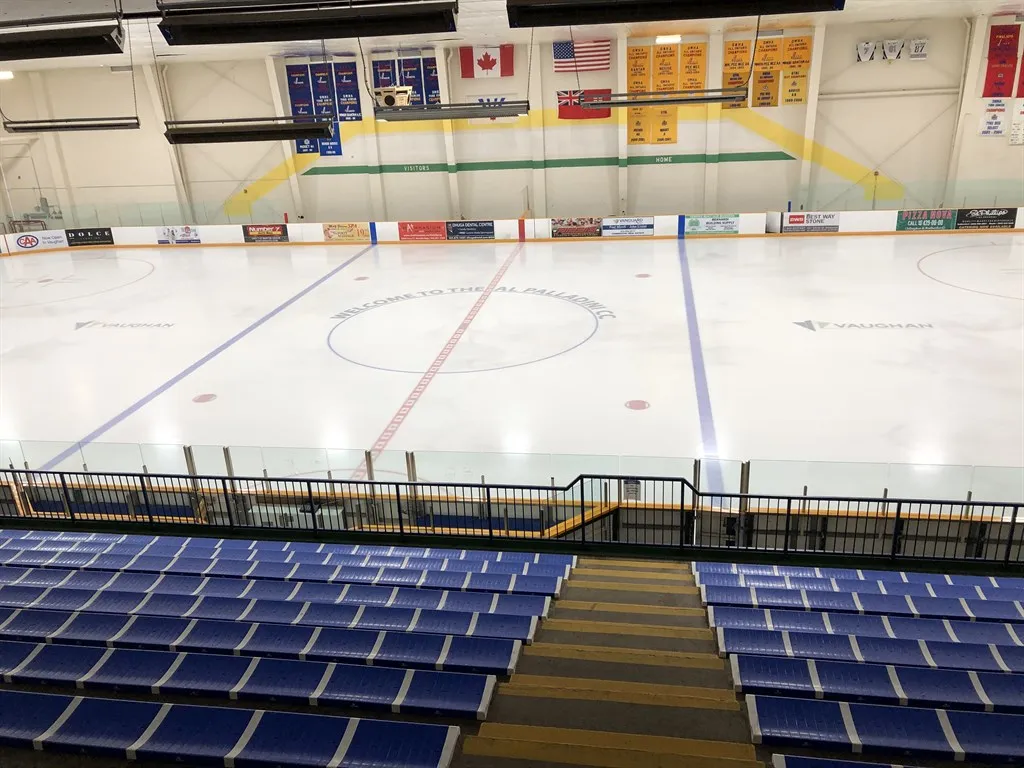 Arena East (A) from the stands: blue seats in the foreground, the full ice sheet, and banners and flags on the far wall. — Al Palladini Community Centre (Vaughan)