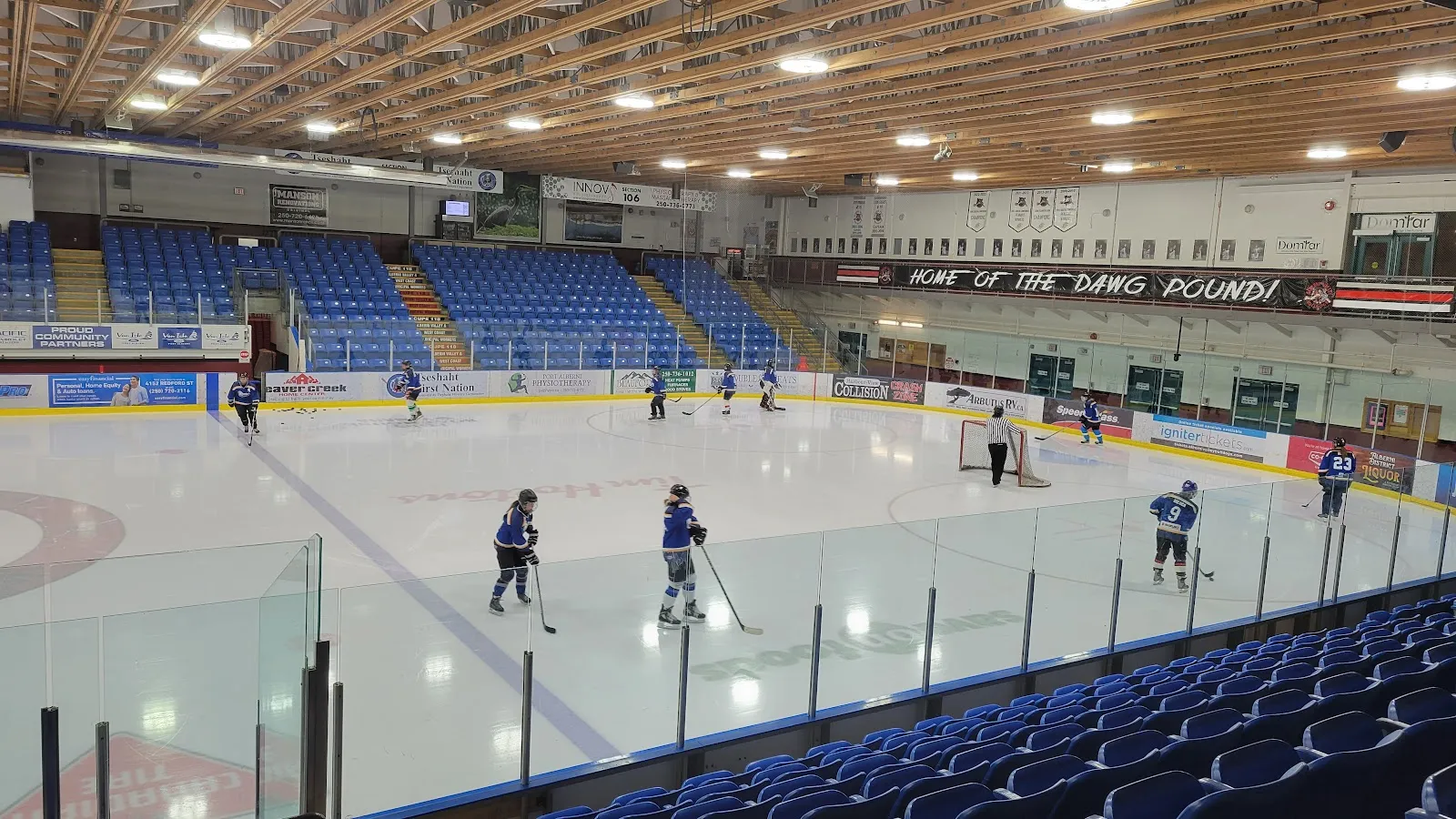 Hielo, gradas y vigas del techo del Alberni Valley Multiplex, con algunos jugadores en la pista — Alberni Valley Multiplex