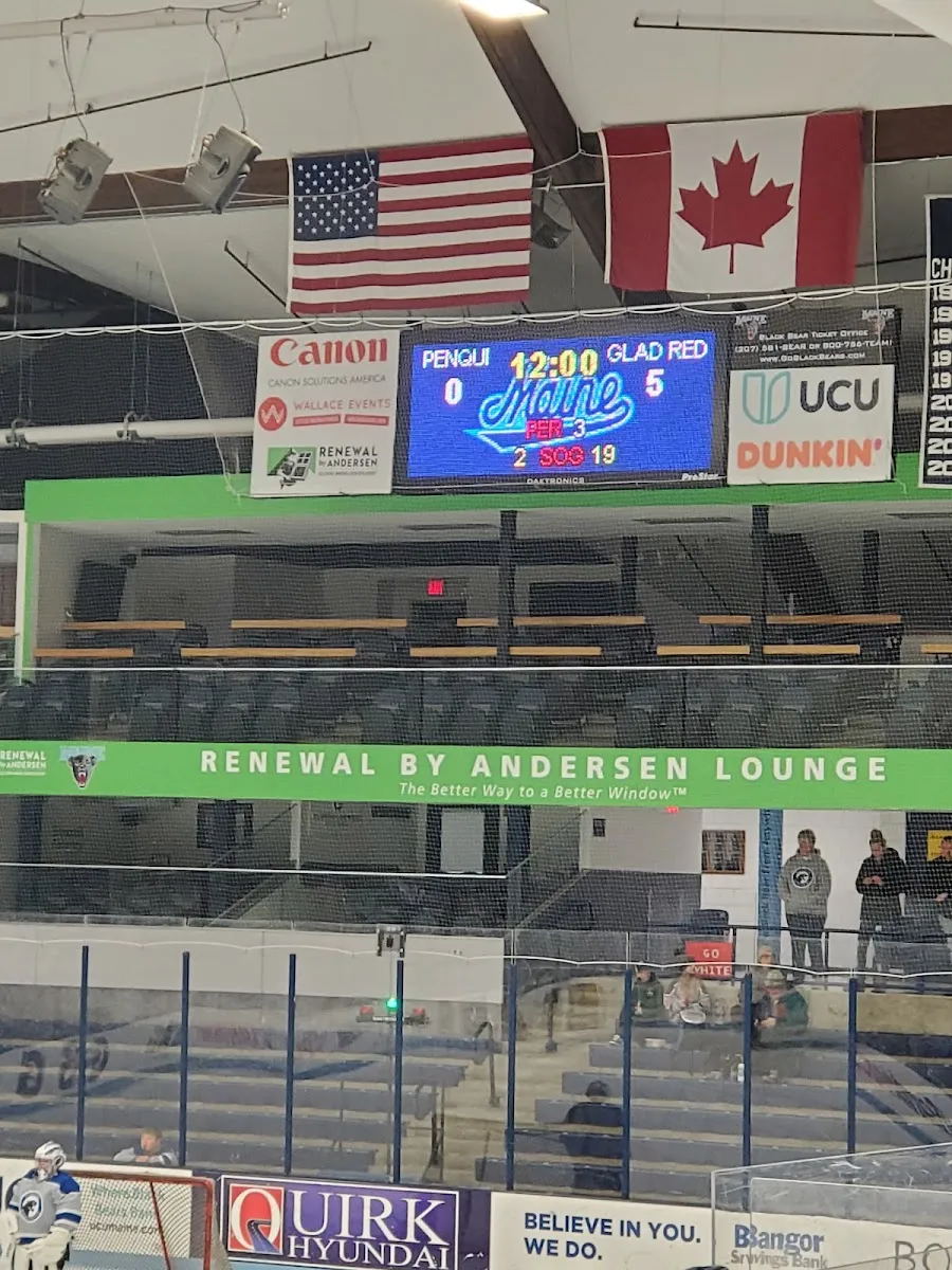 The ice at Alfond Sports Arena during a University of Maine hockey game, seen through the safety netting with the scoreboard and the lounge level above — Alfond Arena