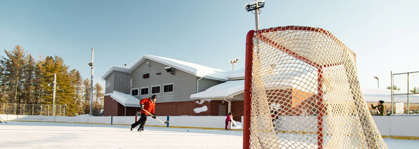 The outdoor rink beside the Alice and Fraser recreation building on a sunny winter day, with a goal in the foreground and a few players in the distance. — Alice and Fraser Outdoor Rink (Laurentian Valley)