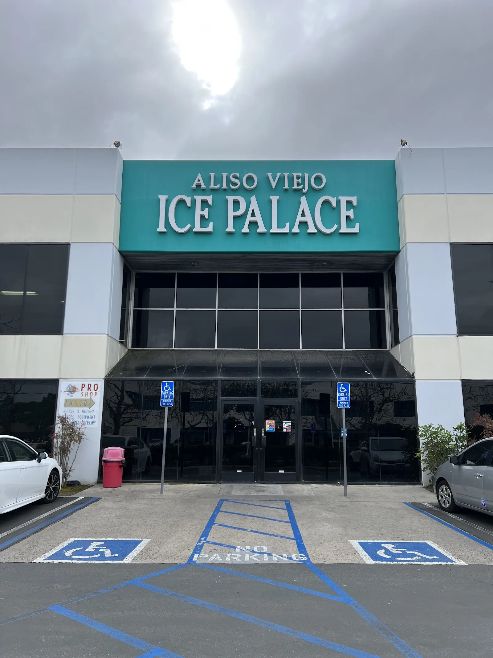 The entrance of Aliso Viejo Ice Palace with its teal name sign above the glass doors and the parking spaces in front — Aliso Viejo Ice Palace
