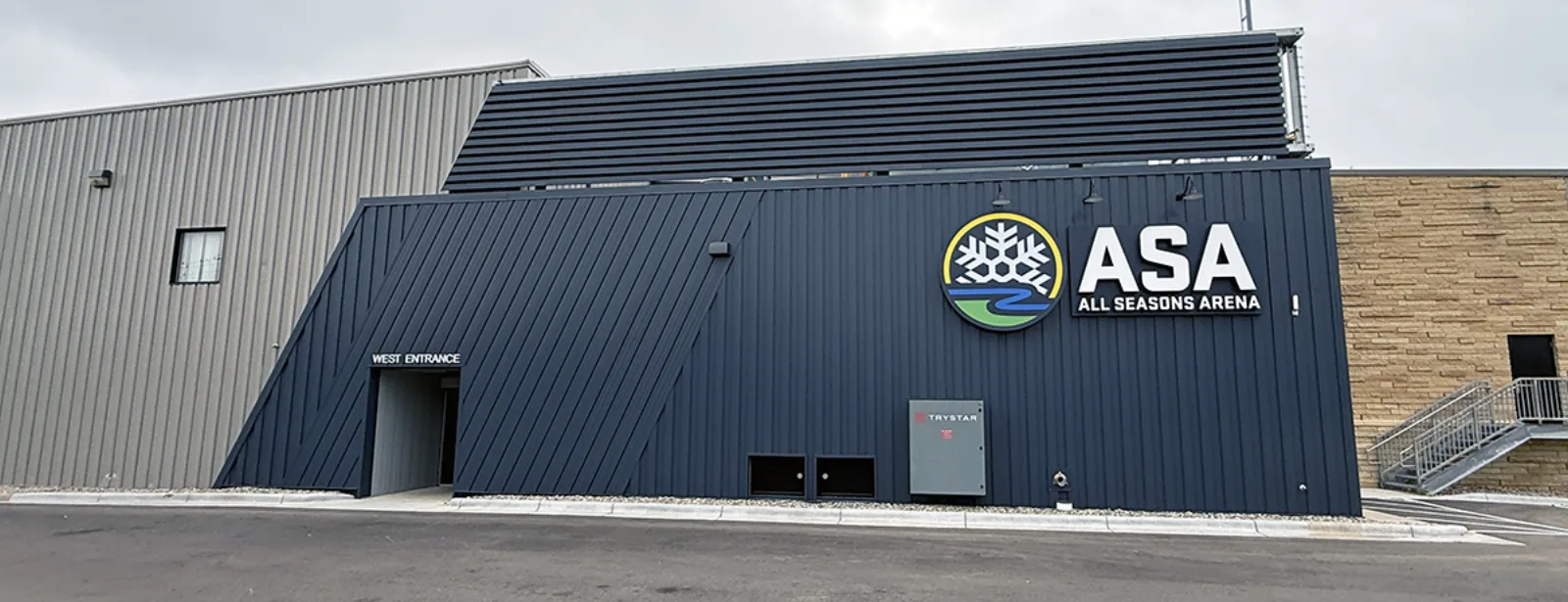 West entrance of the renovated arena building, dark metal-panel facade with a large "ASA All Seasons Arena" wall sign. — All Seasons Arena