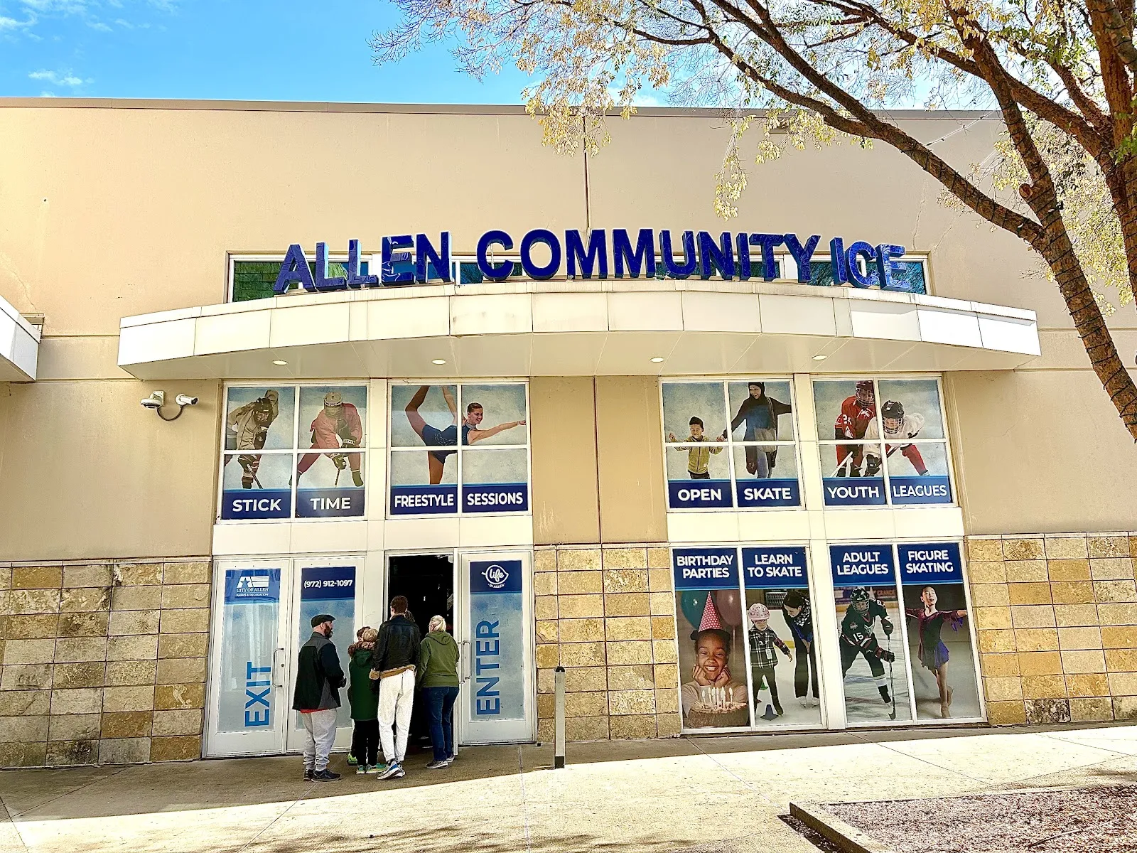 La entrada de la pista desde la calle, con ALLEN COMMUNITY ICE escrito sobre las puertas y carteles de programas en las ventanas. — Allen Community Ice Rink