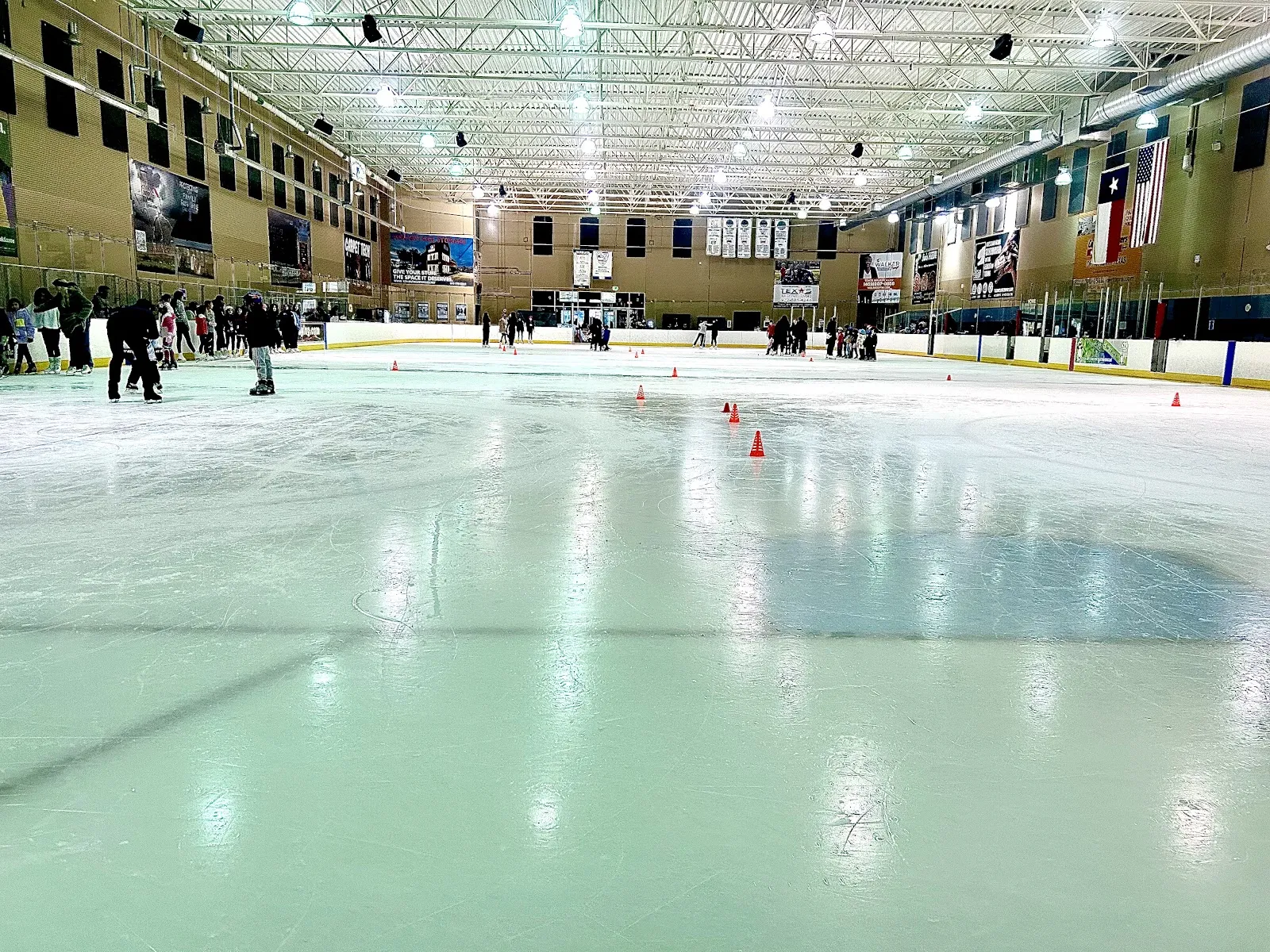 La pista completa vista a la altura del hielo durante una sesión pública, con banderines y banderas en la pared del fondo. — Allen Community Ice Rink