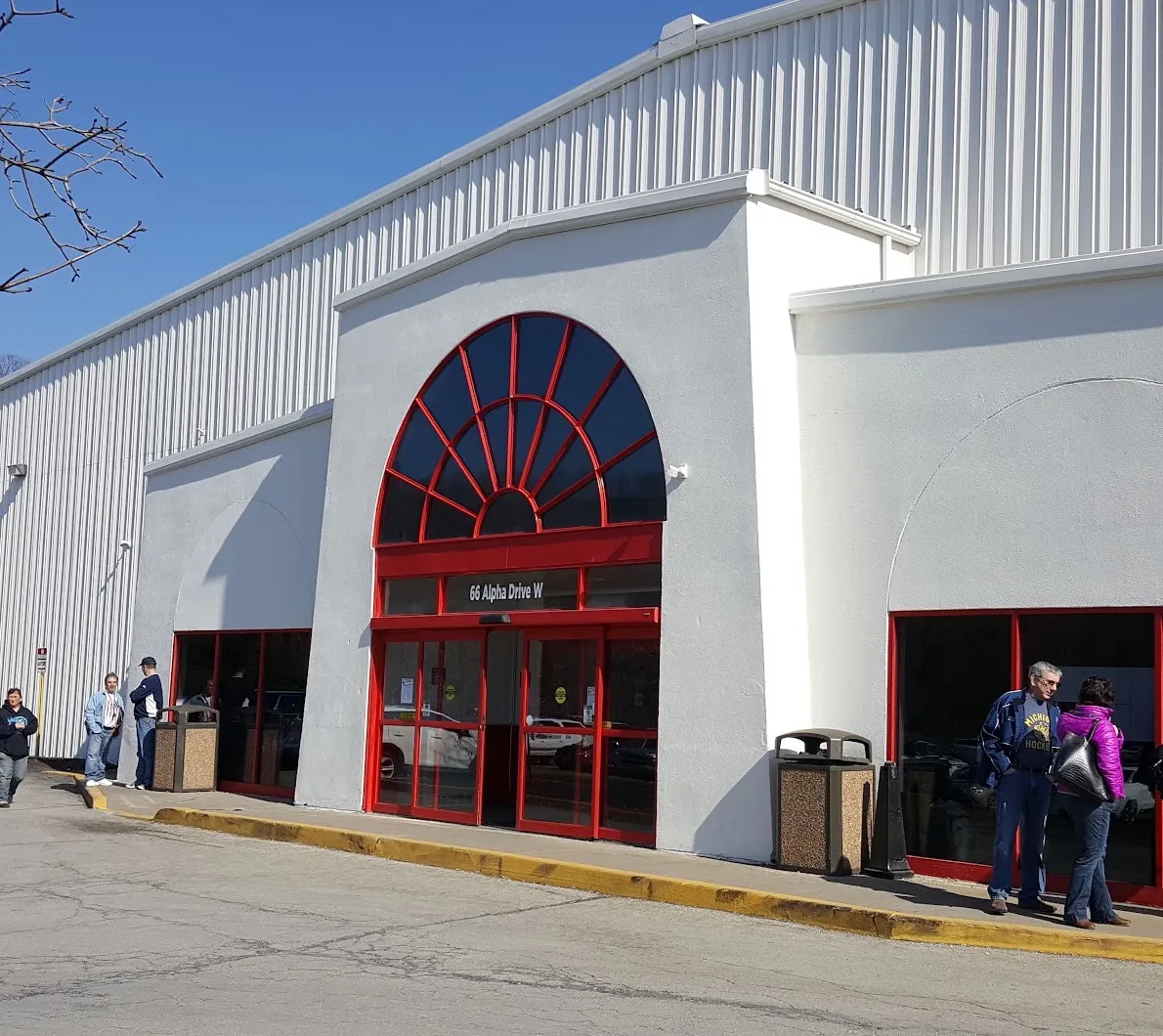 The Alpha Ice Complex entrance at 66 Alpha Drive W: a white stucco front with a red-framed fan window over the doors, below the long metal rink hall — Alpha Ice Complex