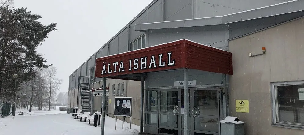 The entrance of Älta ishall under its red sign, in the snow — Älta ishall