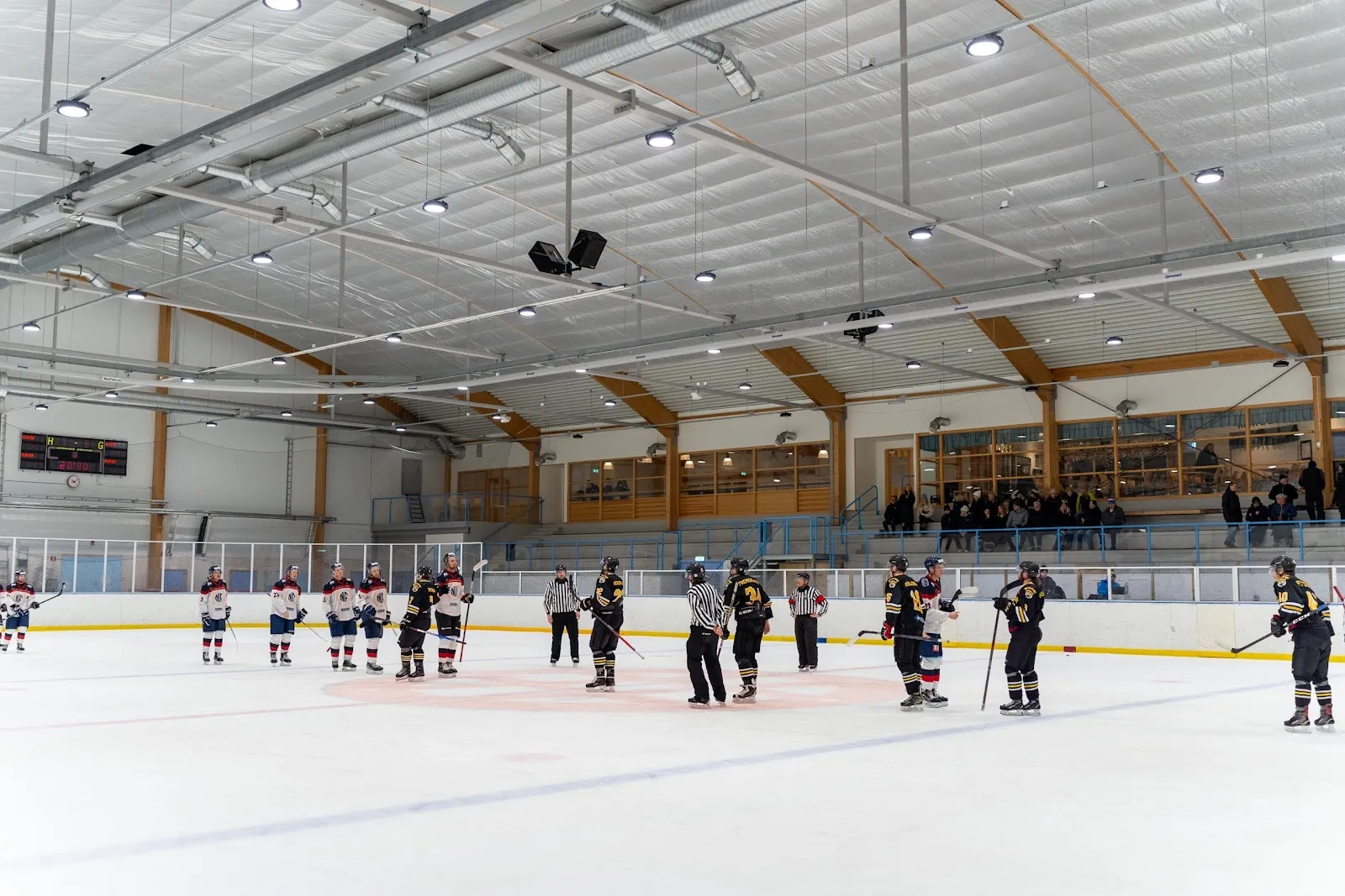 A group of young players practising on the ice at Älta ishall, seen from the boards across the sheet under the bright white roof. — Älta ishall