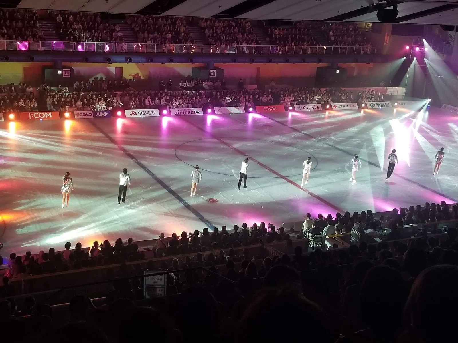 An ice show on the rink at Amagasaki Sports Forest, with the lit ice, performers on it and the crowd packing the stands around. — Amagasaki Sports Forest Ice Rink