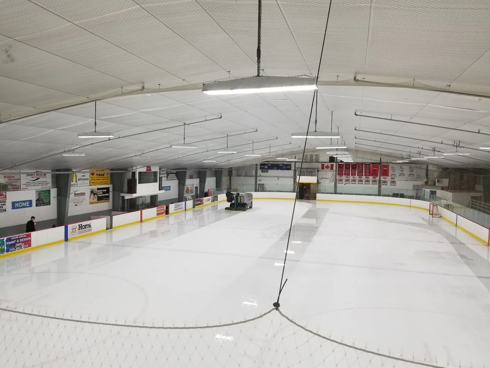 The empty Angus ice from one end, under a low white ceiling with sponsor boards along the sides. — Angus Recreation Centre
