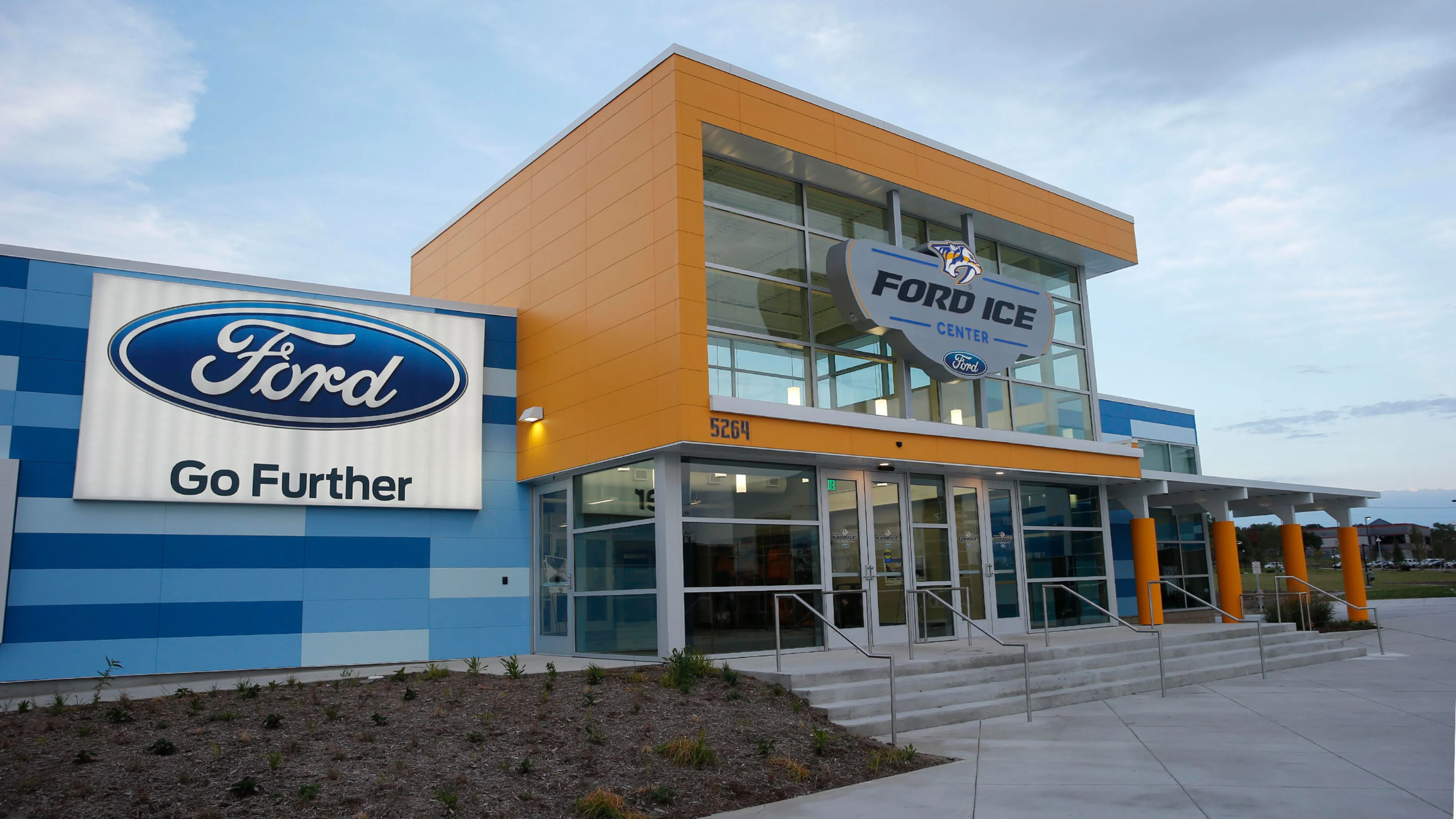 Lit entrance canopy beneath the orange and blue facade — Ford Ice Center – Antioch