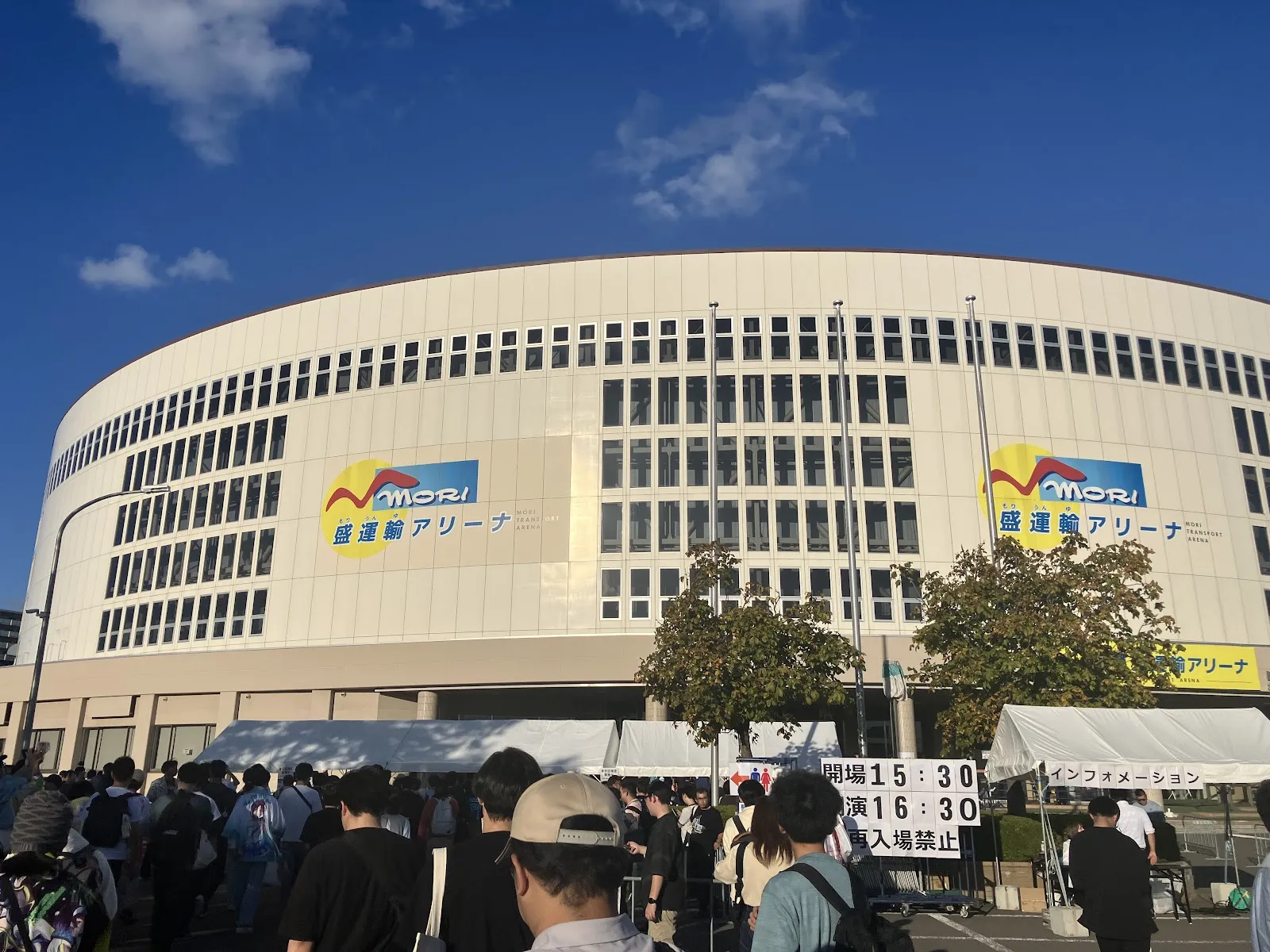 The curved cream-coloured facade of Mori Transport Arena in Aomori under a blue sky, with the arena's logo banners on the wall and a crowd queueing outside. — Aomori Prefectural Skating Rink (Mori Transport Arena)