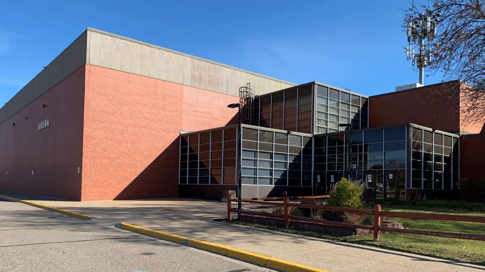 The red-brick Apple Valley Sports Arena with its glass-walled entrance and an Arena sign on the tall brick wall. — Apple Valley Sports Arena