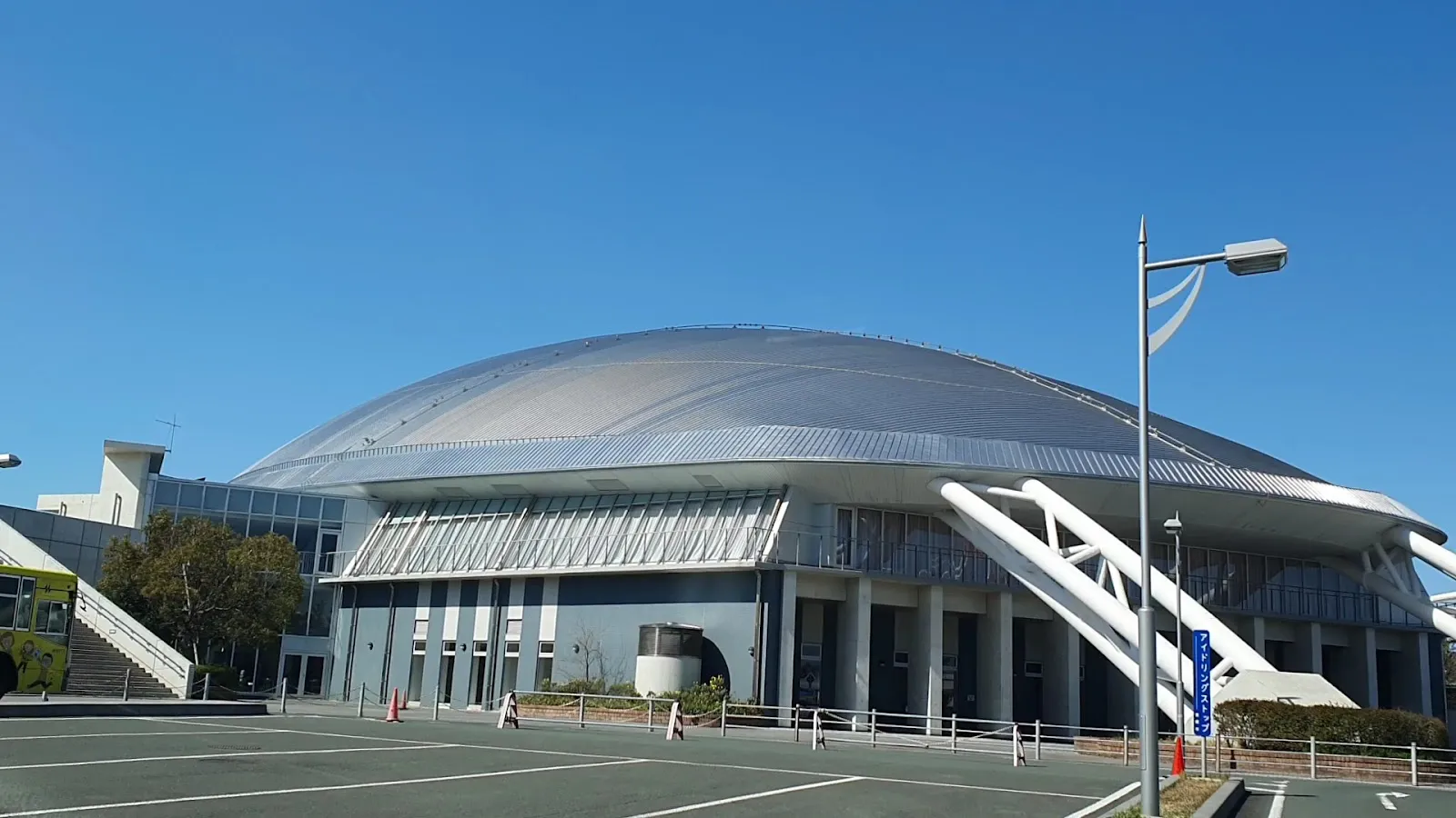 晴れた日に駐車場越しに見た、アクアリーナ豊橋の銀色のドーム屋根と白い支柱。 — Aquarena Toyohashi