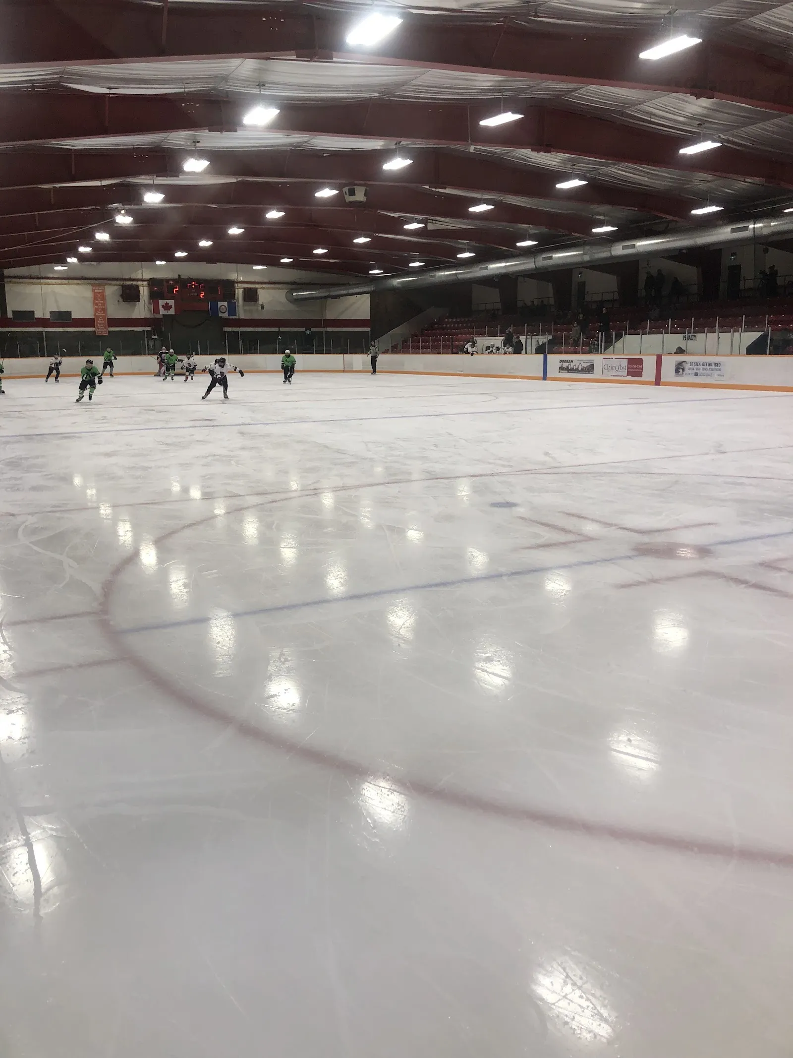 The ice at the Archie Dillon Sportsplex with skaters at the far end, the roof trusses and lights above and a red circle in the foreground. — Archie Dillon Sportsplex