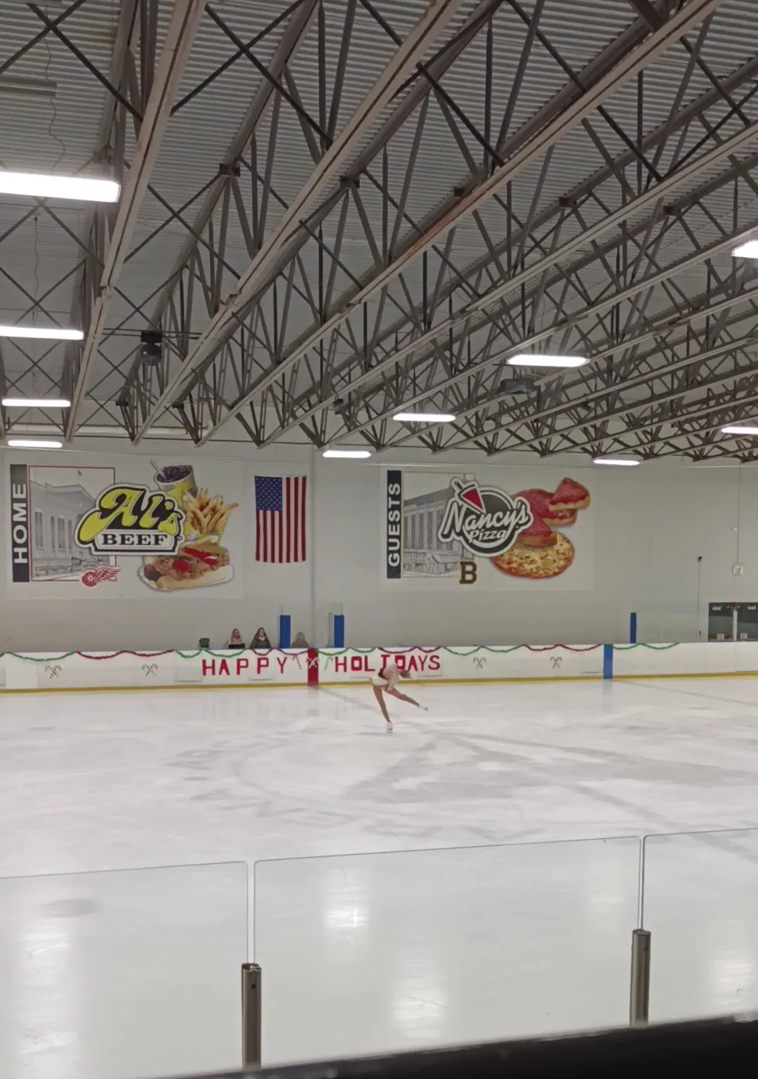 La pista de Arctic Ice Arena vista a través del cristal, con un patinador solitario a lo lejos y los murales de patrocinadores de pizza y carne en el muro del fondo — Arctic Ice Arena (Orland Park)