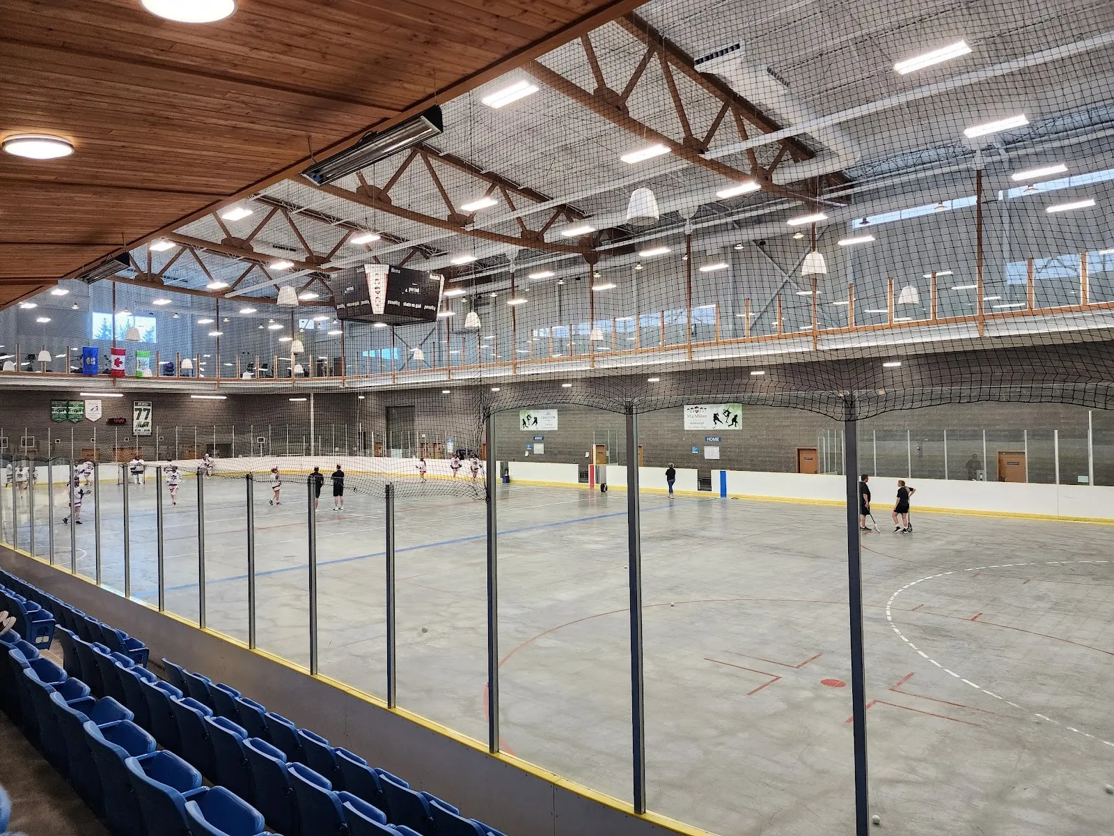 A wide view of the sheet from the glass with a timber-ribbed ceiling and a lit upper walkway, a few skaters spread across the ice. — Ardrossan Recreation Complex
