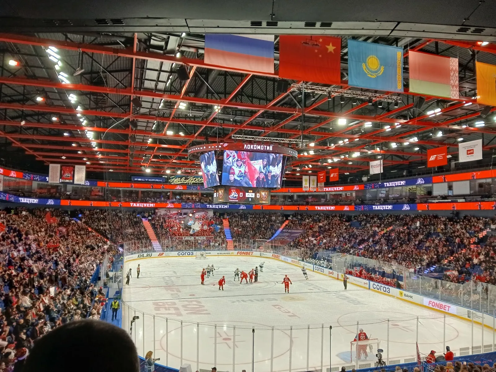 The ice of Arena 2000 Lokomotiv in Yaroslavl seen from the stands during a match, with the scoreboard, the flags and the full stands around the rink. — Arena 2000 Lokomotiv