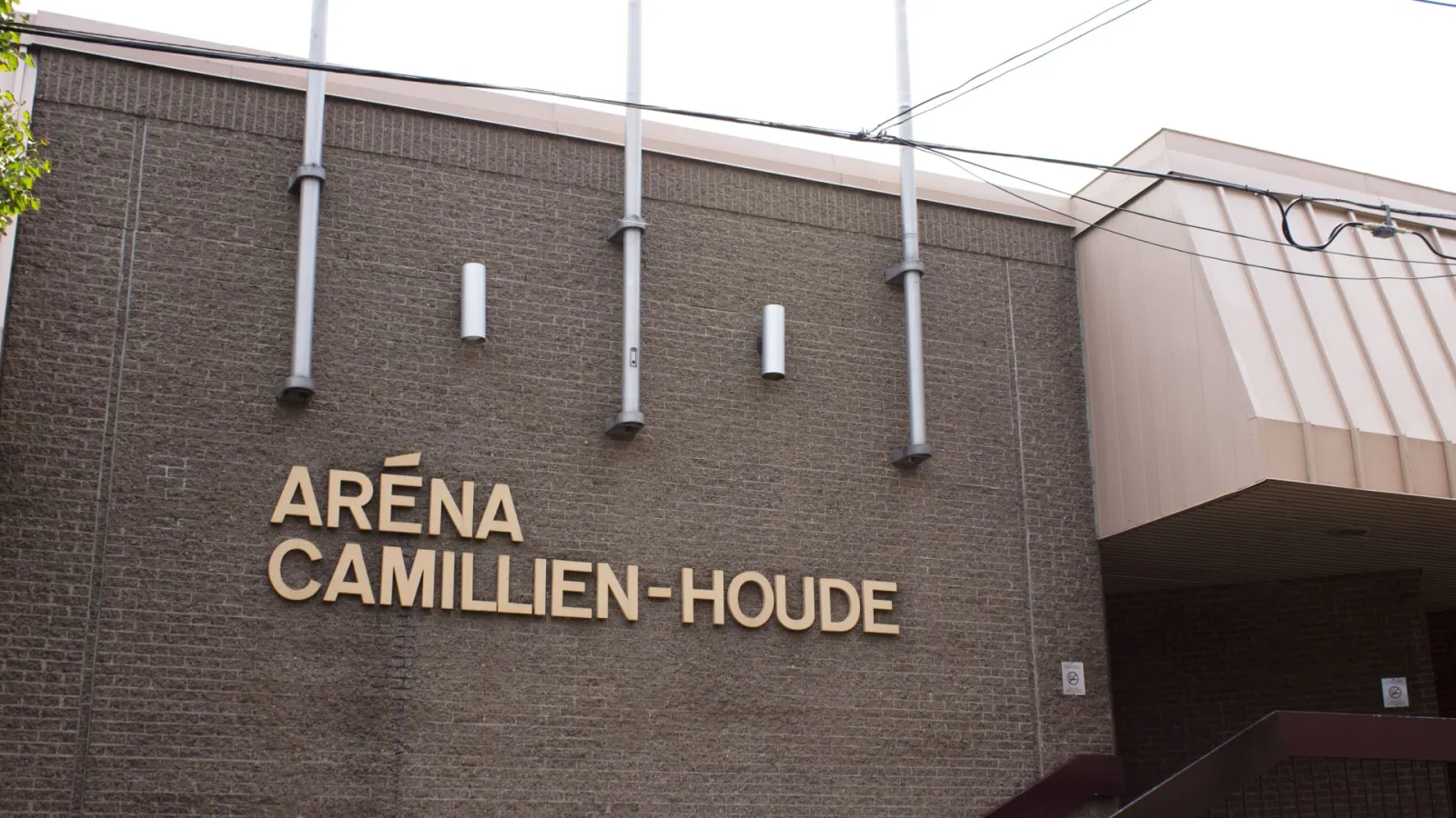 La façade de brique de l’Aréna Camillien-Houde avec le lettrage en relief « ARÉNA CAMILLIEN-HOUDE », vue d’en bas contre la ligne du toit. — Aréna Camillien-Houde