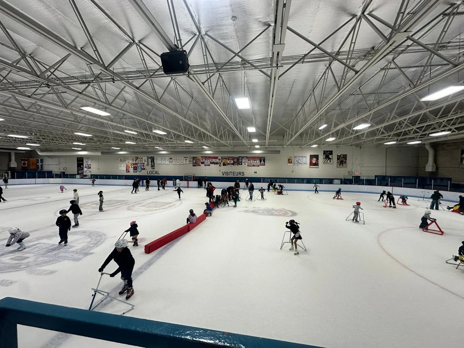 Una práctica estilo hockey sobre trineo en una pista amplia, con jugadores repartidos por el hielo alrededor de una línea de entrenamiento roja bajo un techo de armaduras de acero. — Aréna Chaumont