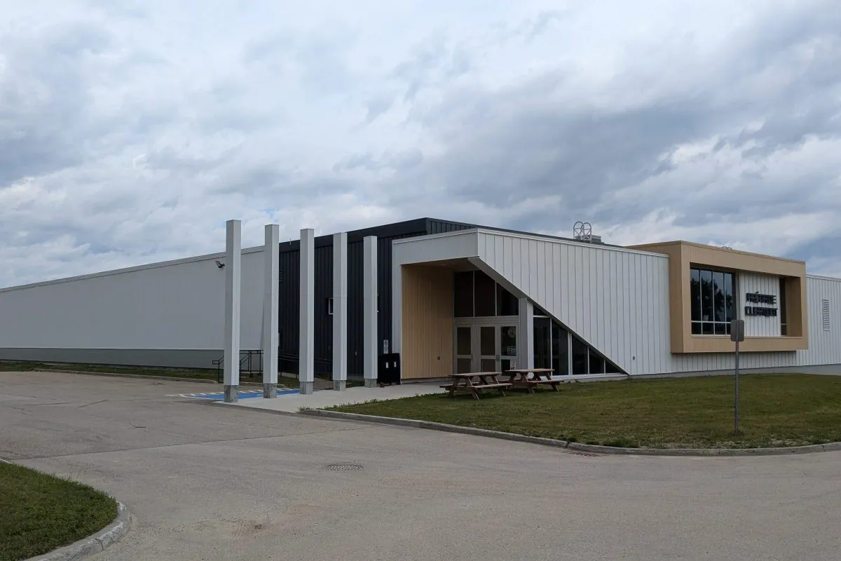 Le bâtiment de métal blanc de l’aréna, avec une rangée de hautes colonnes blanches et un volume d’angle revêtu de bois à l’entrée. — Aréna de Clermont