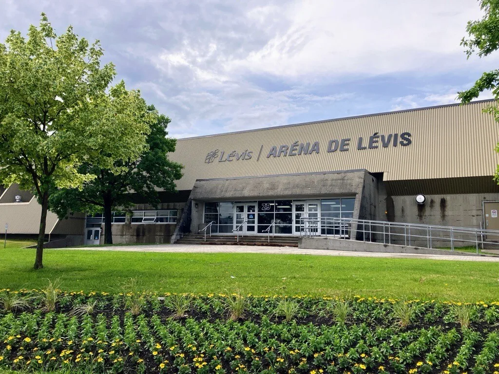 L'aréna de Lévis vu depuis sa pelouse, un long bâtiment avec l'enseigne de Lévis le long de la façade. — Aréna de Lévis