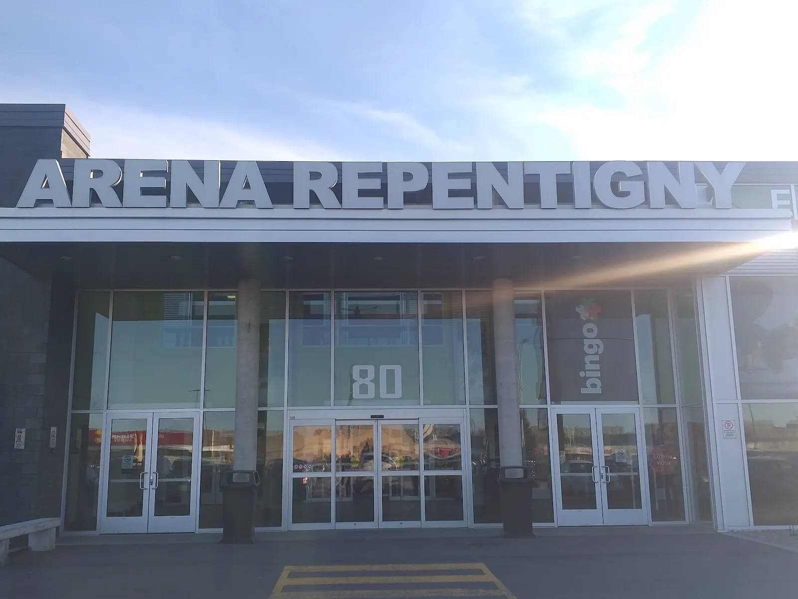 La entrada de la Aréna Repentigny, con el nombre de la arena en letras grandes sobre las puertas de vidrio y el número 80 de la calle. — Aréna de Repentigny
