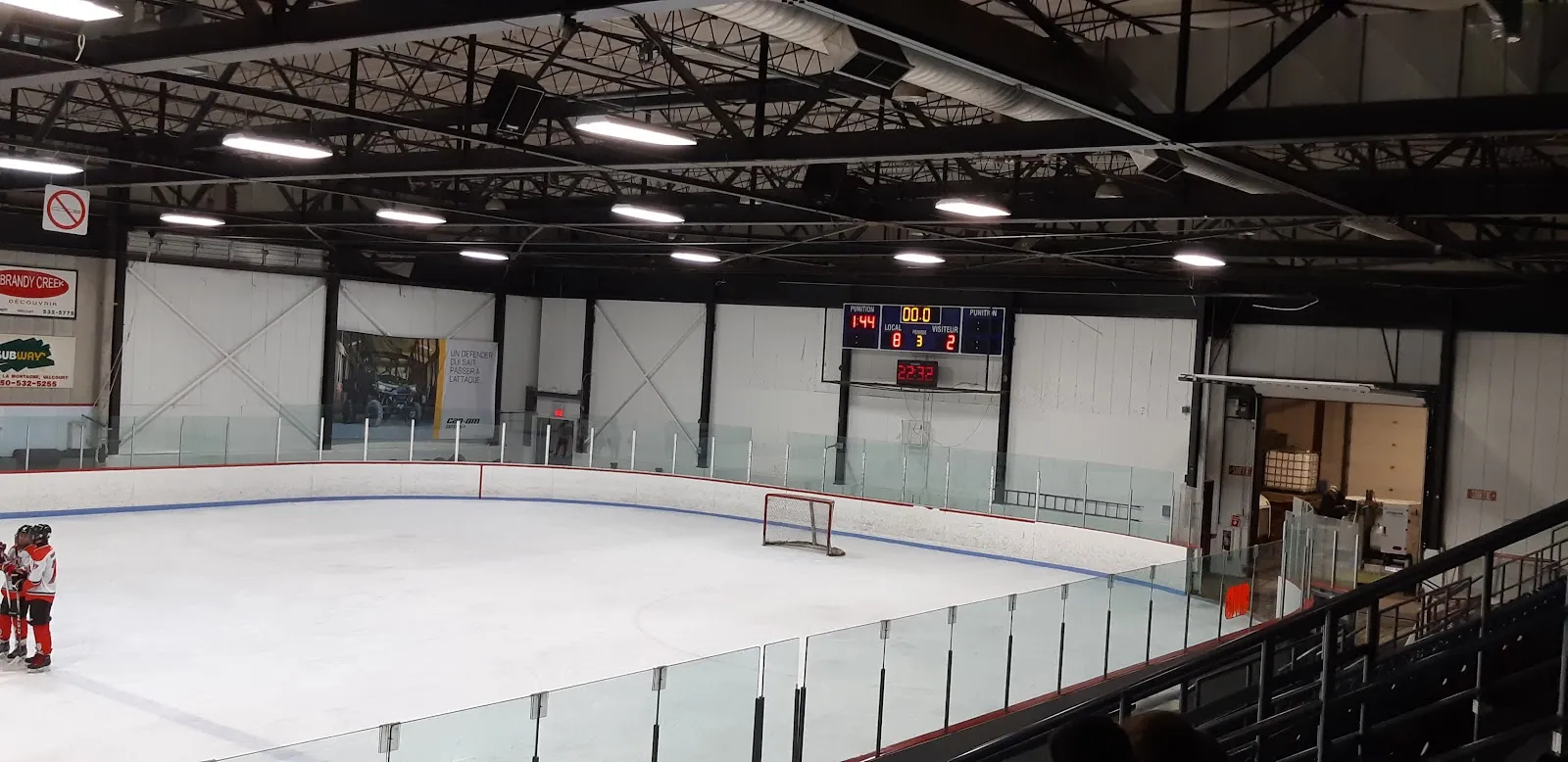 The ice surface of the Aréna de Valcourt seen from the stands, with the glass, the scoreboard and the banners along the boards — Aréna de Valcourt