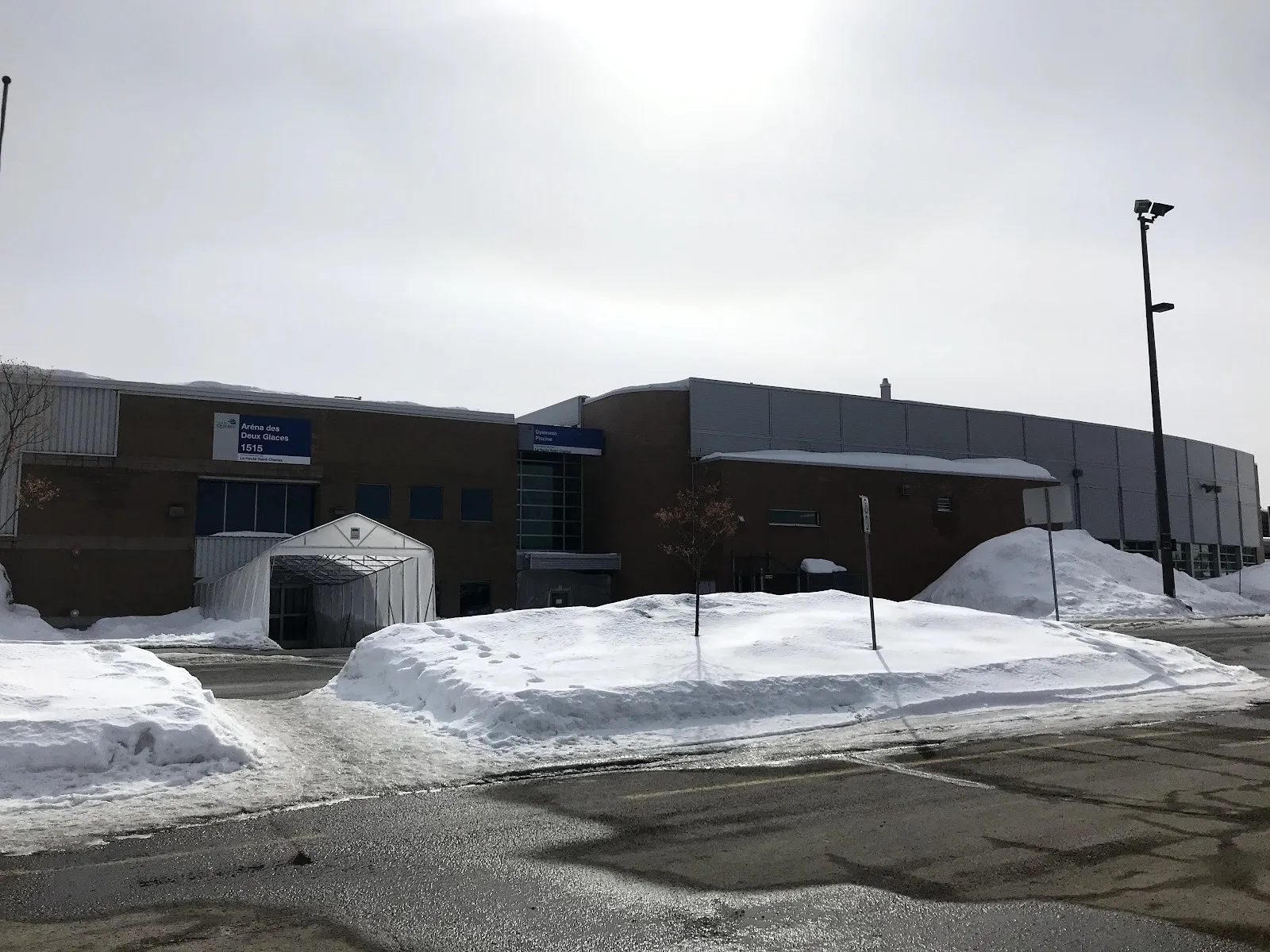 La façade de brique de l’Aréna des Deux Glaces à Val-Bélair, à Québec, avec l’enseigne de la Ville portant le nom au-dessus de l’entrée, en hiver — Aréna des Deux Glaces