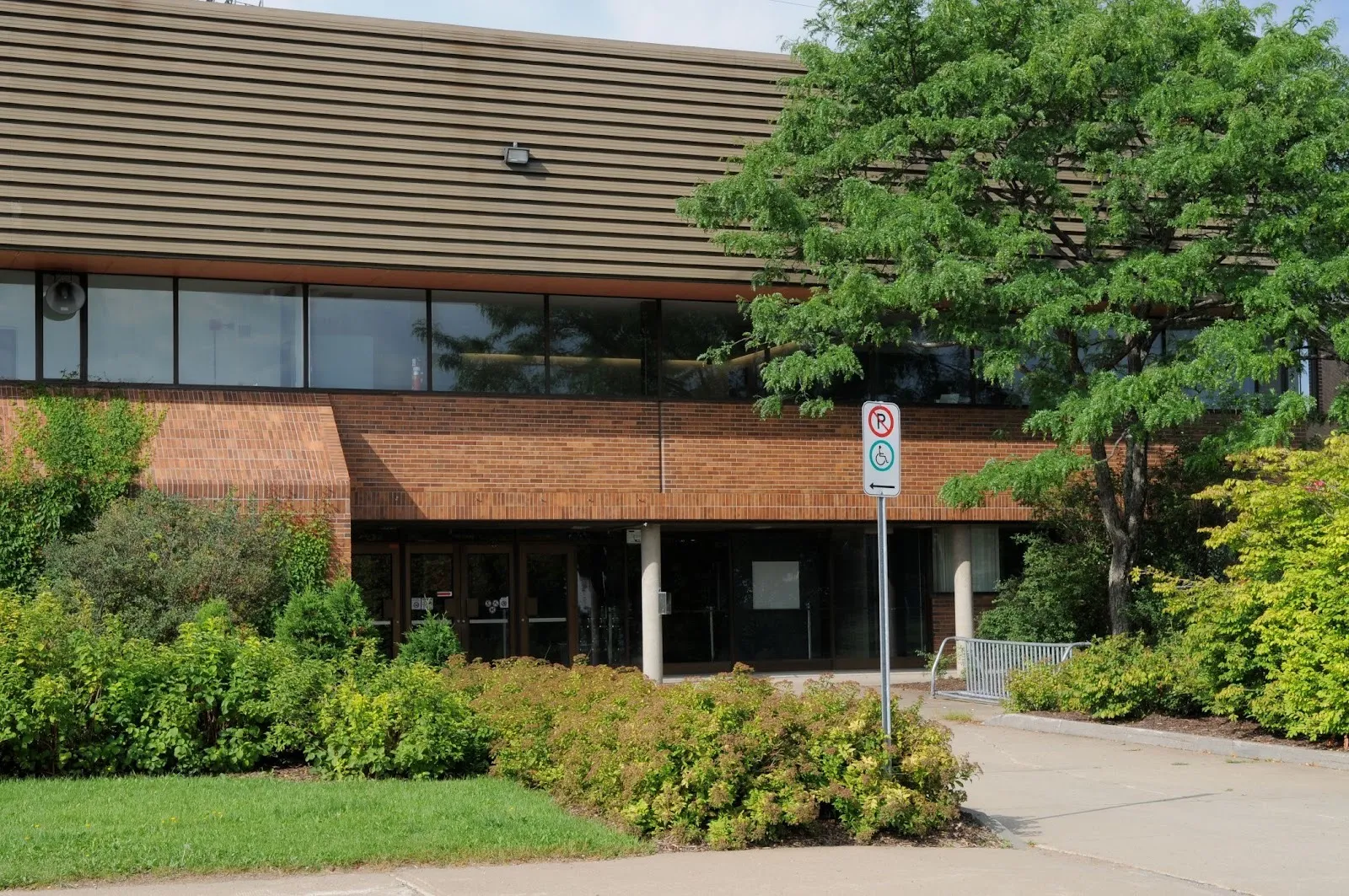The brick and glass entrance of the Aréna Gaétan-Duchesne on avenue d'Alembert in Québec, framed by shrubs and a tree — Aréna Gaétan-Duchesne