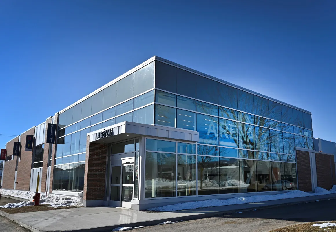 The arena's two-storey glass front under a winter sky, with ARÉNA lettering behind the glazing. — Aréna Luc-et-Marie-Claude