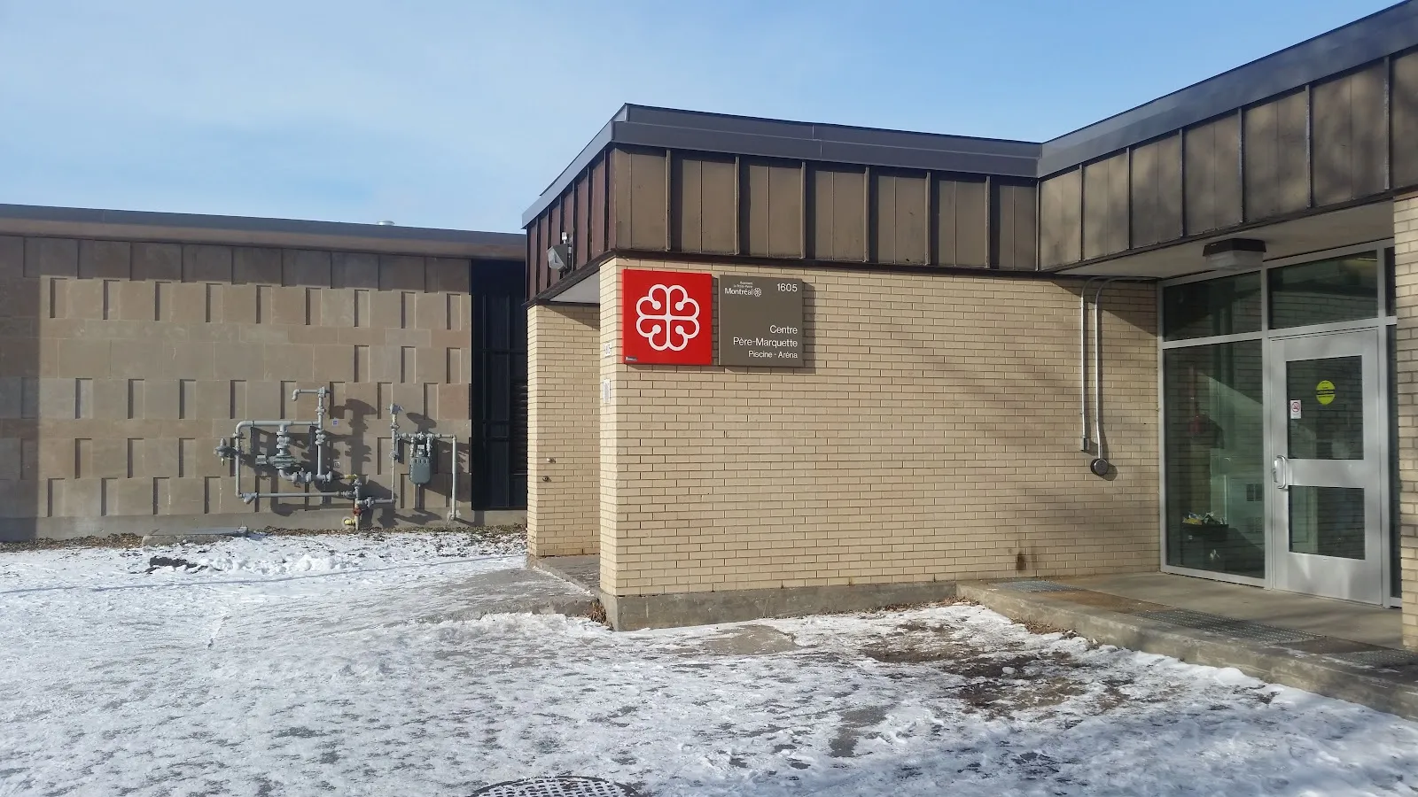 L'entrée en brique du Centre Père-Marquette par temps de neige, avec l'emblème de Montréal et la plaque « 1605, Centre Père-Marquette, Piscine - Aréna » à côté des portes vitrées. — Aréna Père-Marquette