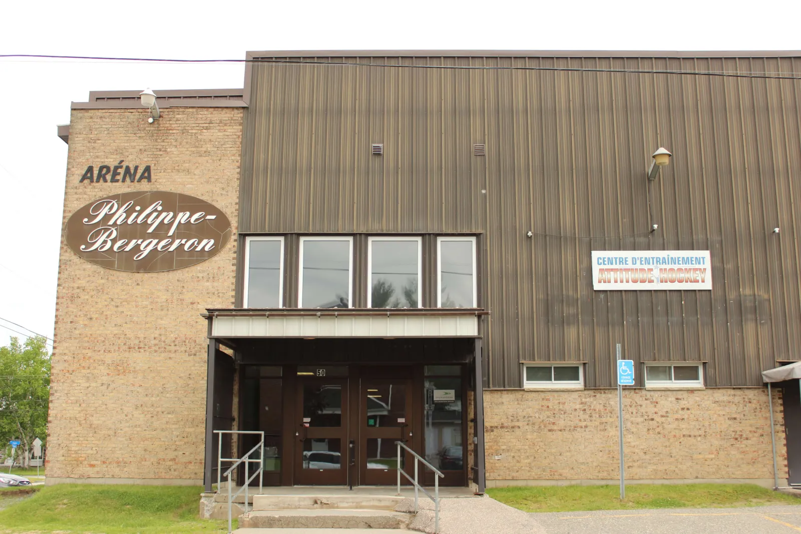 The brick and brown metal front of the arena, with an oval Aréna Philippe-Bergeron sign beside the canopied entrance and its stairs. — Aréna Philippe-Bergeron
