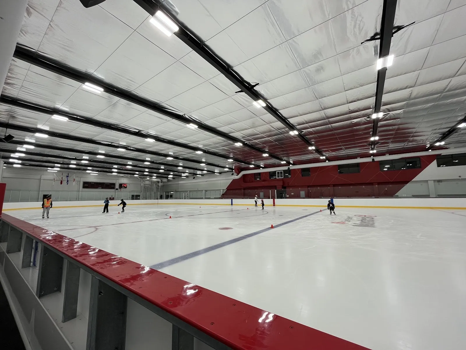Une glace de l’Aréna Raymond-Bourque vue des bandes rouges, avec un groupe d’initiation au patinage sur la glace sous la galerie supérieure aux murs rouges — Aréna Raymond-Bourque