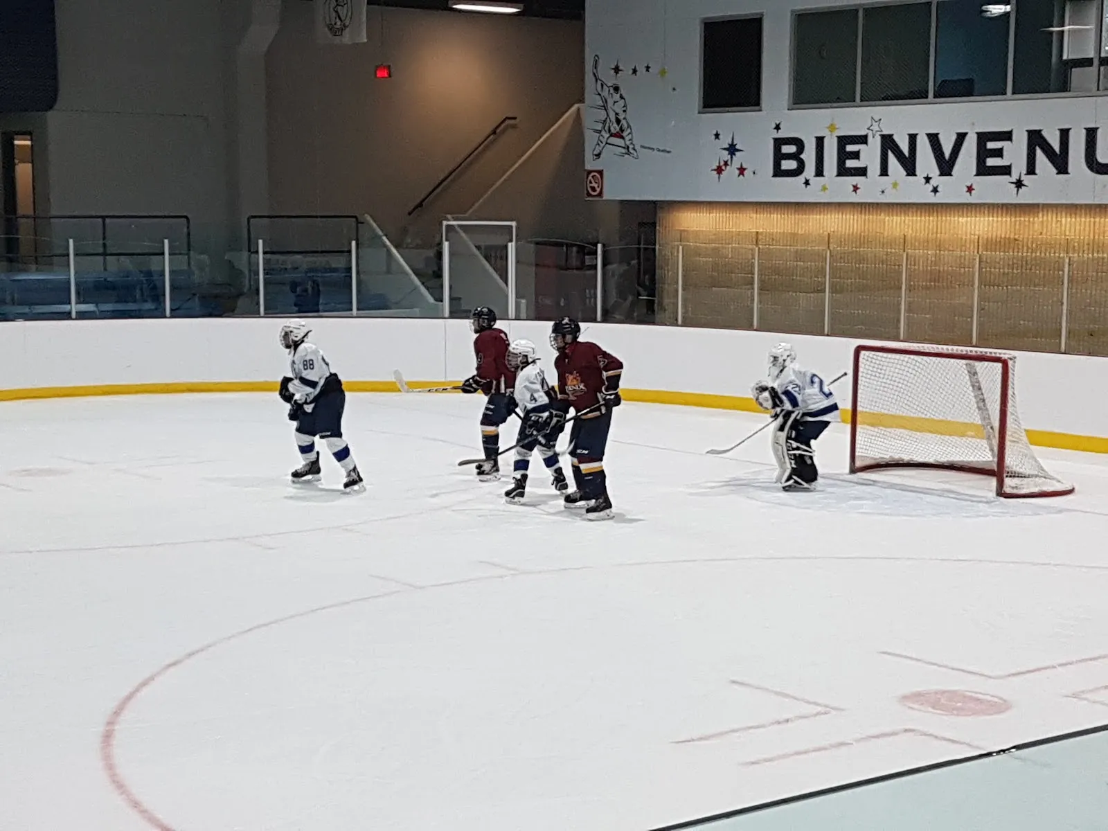 La surface de glace de l’Aréna Roch-Lasalle avec quelques patineurs près du filet au fond et une enseigne « Bienvenue » sur le mur derrière les bandes. — Aréna Roch-Lasalle