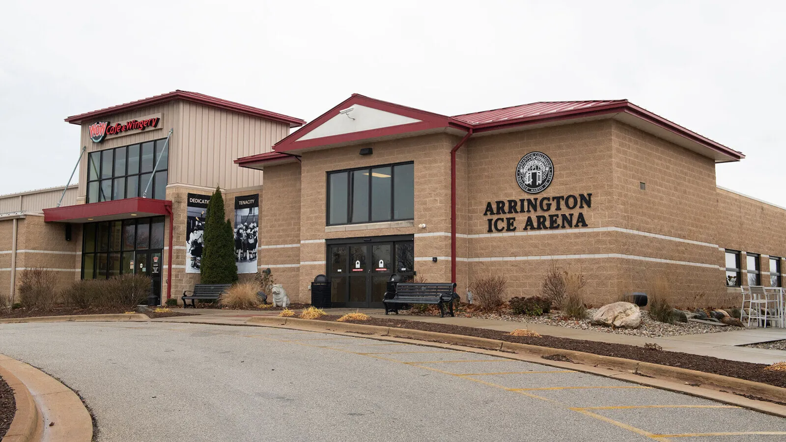 The arena's tan block and glass entrance with a red gabled roof and the sign "Arrington Ice Arena" beside the doors. — Arrington Ice Arena