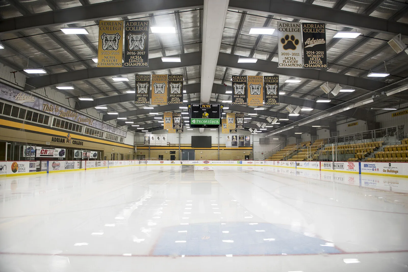 The empty sheet from one end, with black and gold championship banners hanging from the roof beams and seating along both sides. — Arrington Ice Arena