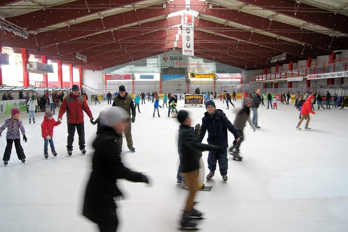 A public skating session at the Wedemark ice stadium, skaters scattered across the ice under the red-trimmed roof. — ARS Arena Eisstadion Mellendorf