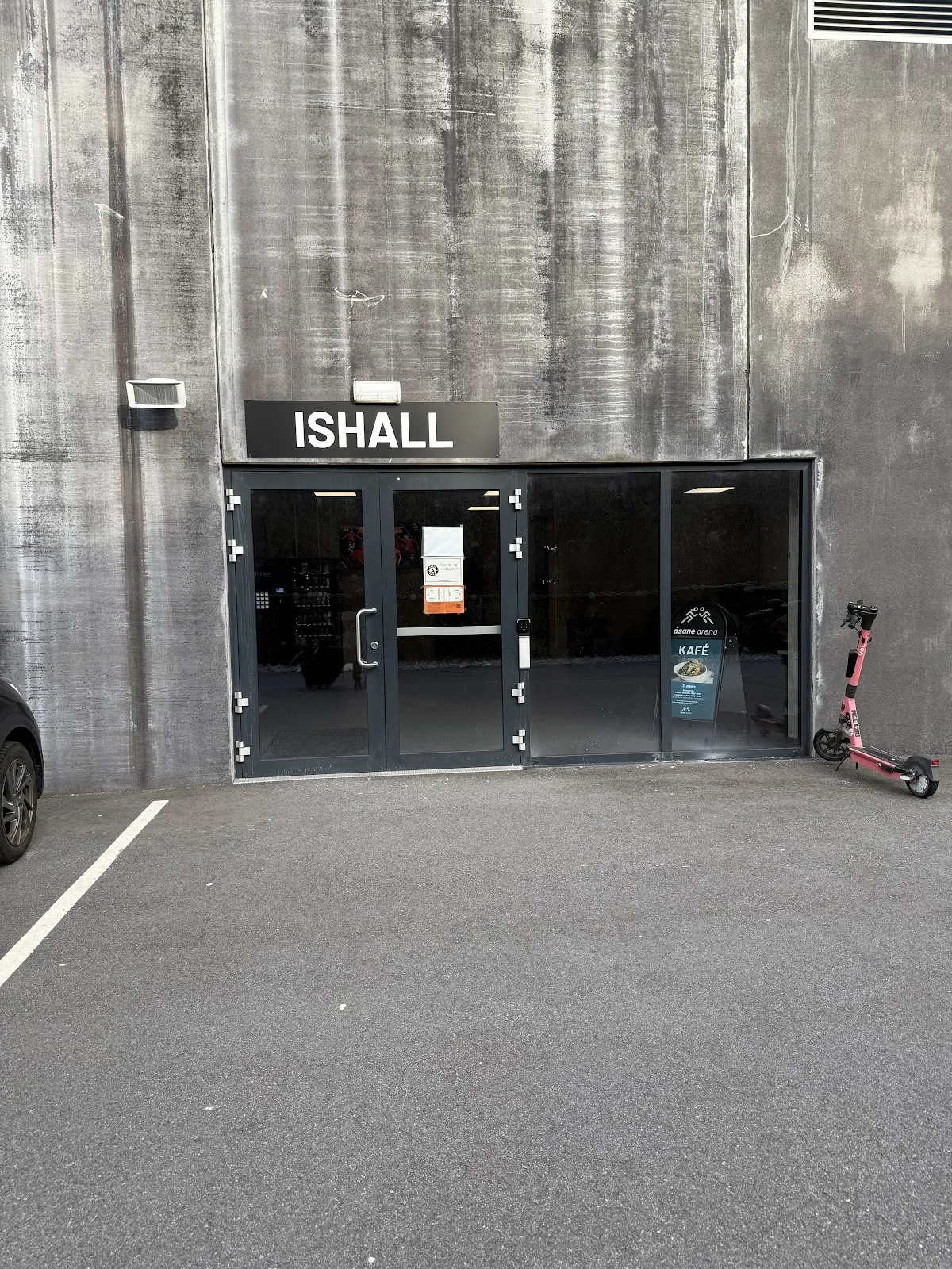 The ISHALL entrance in the grey concrete wall of Åsane Arena, with the cafe sign beside the glass door. — Åsane Arena (ice hall)