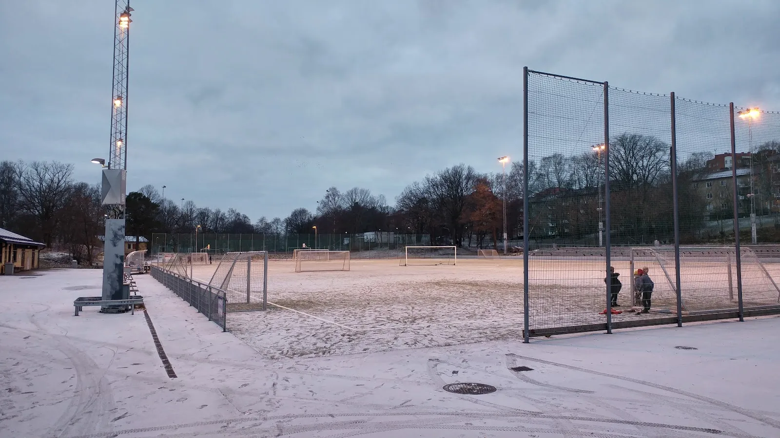 Aspuddens idrottsplats at dusk with snow on the ground and the floodlights lit — Aspuddens skridskois