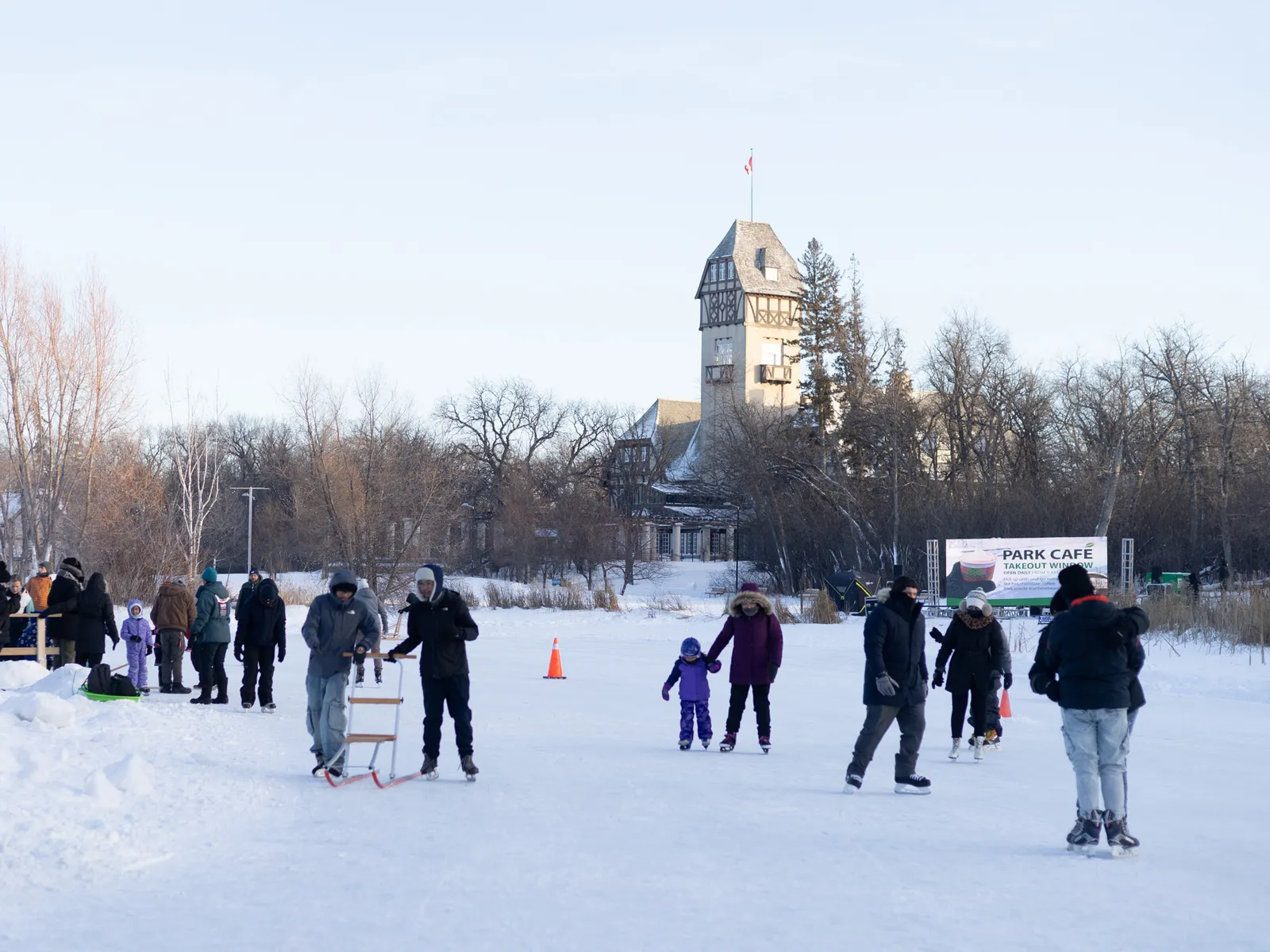 Skaters on the Riley Family Duck Pond rink at Assiniboine Park in Winnipeg on a winter afternoon, with the Pavilion tower behind the trees. — Assiniboine Park Riley Family Duck Pond Rink