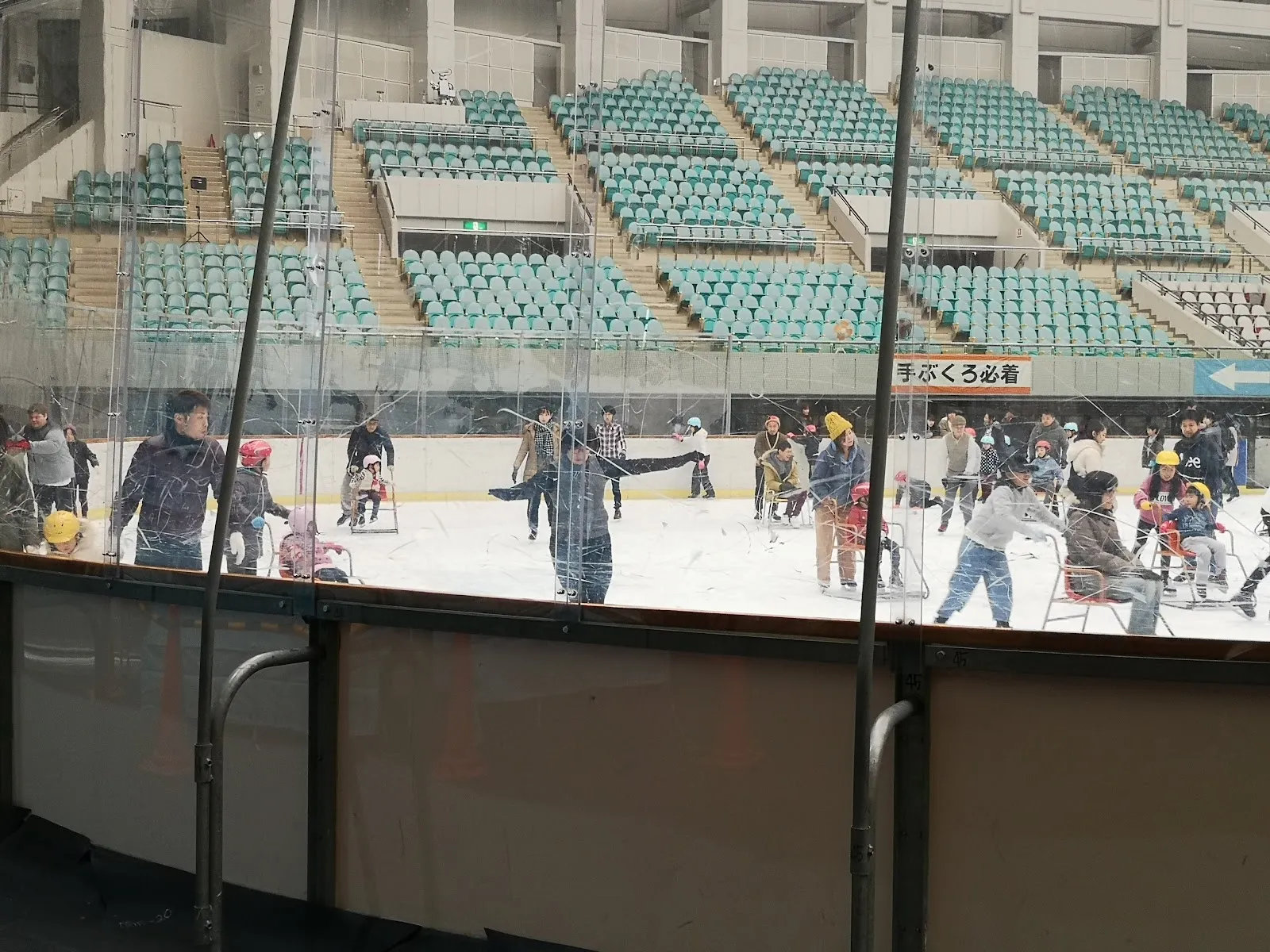 Skaters on the ice of the rink at Asue Osaka Pool, seen from the rink-side with the stands behind. — Asue Osaka Pool Ice Skating Rink